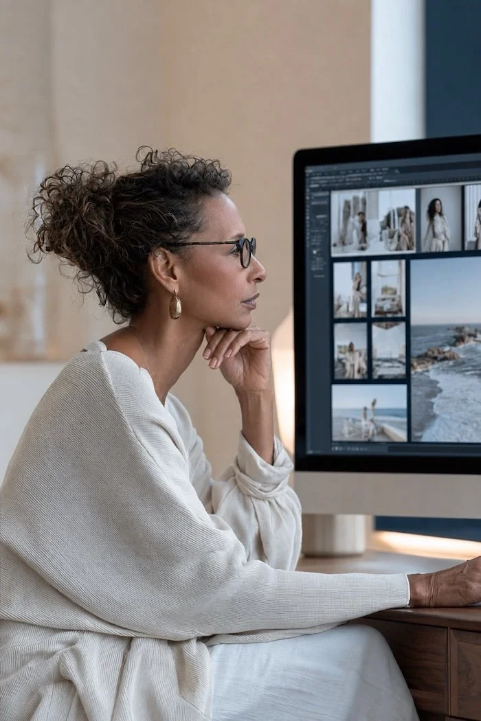 Woman reviewing a grid of professional brand photos on a large monitor, evaluating images as part of an AI brand photography art direction process