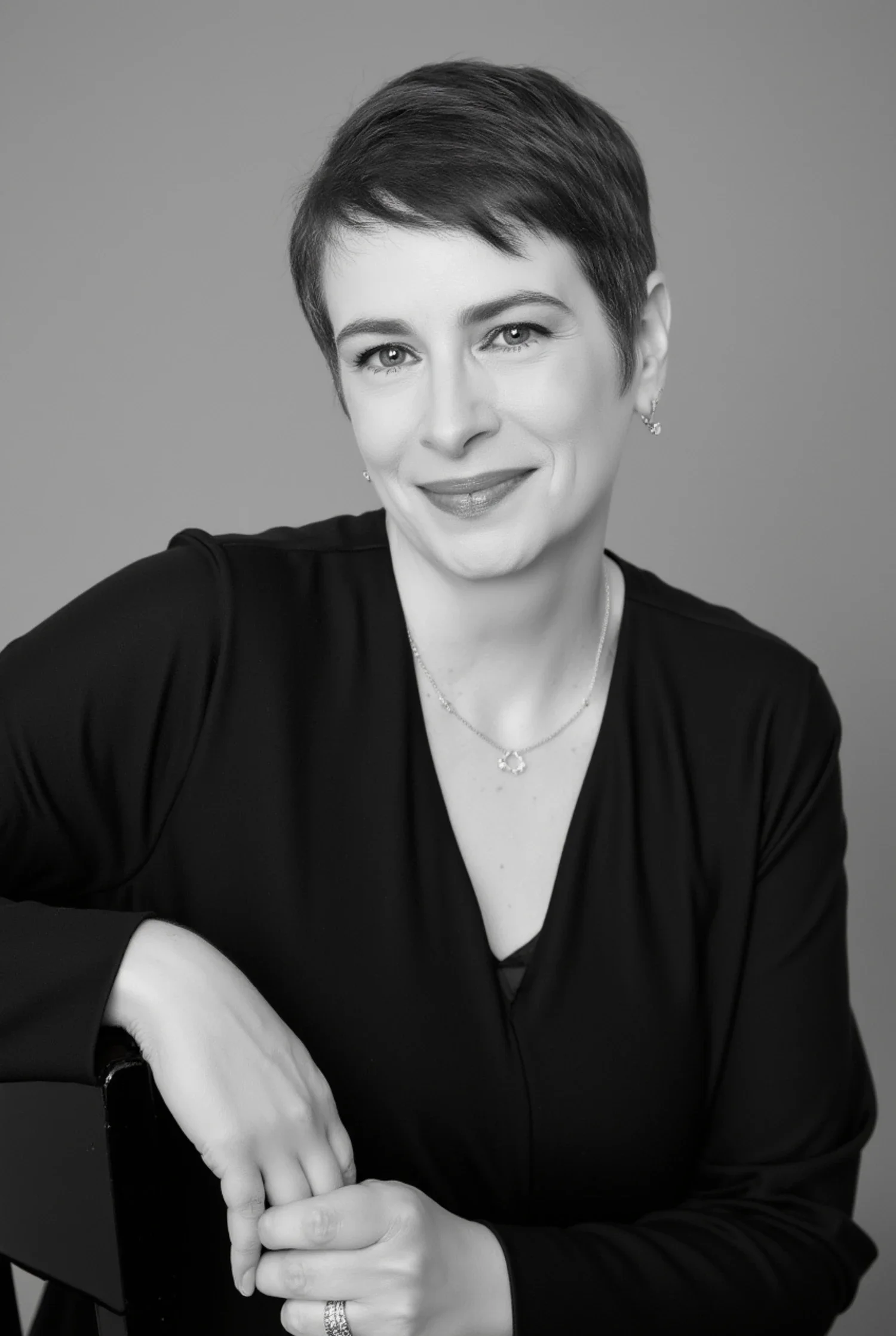 Meg Desjarlais with a relaxed smile, hands resting on a chair arm — black and white example of the ai brand photography she creates.