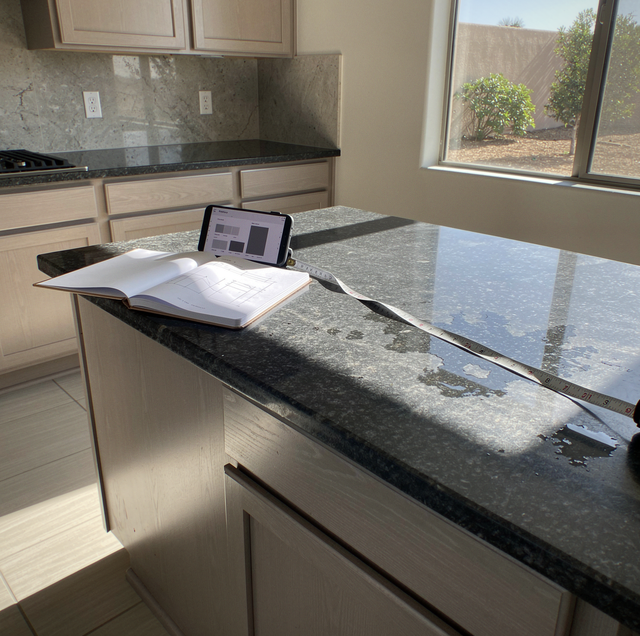 A tablet and notebook sit on a dark granite kitchen counter near a window overlooking a fence.