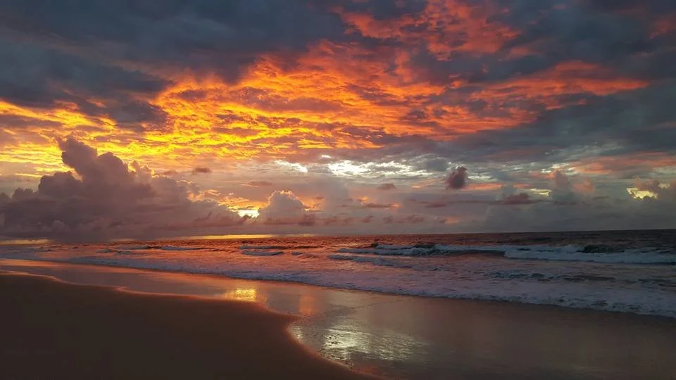 Sunset over the ocean with colorful clouds and wet sandy beach in the foreground.