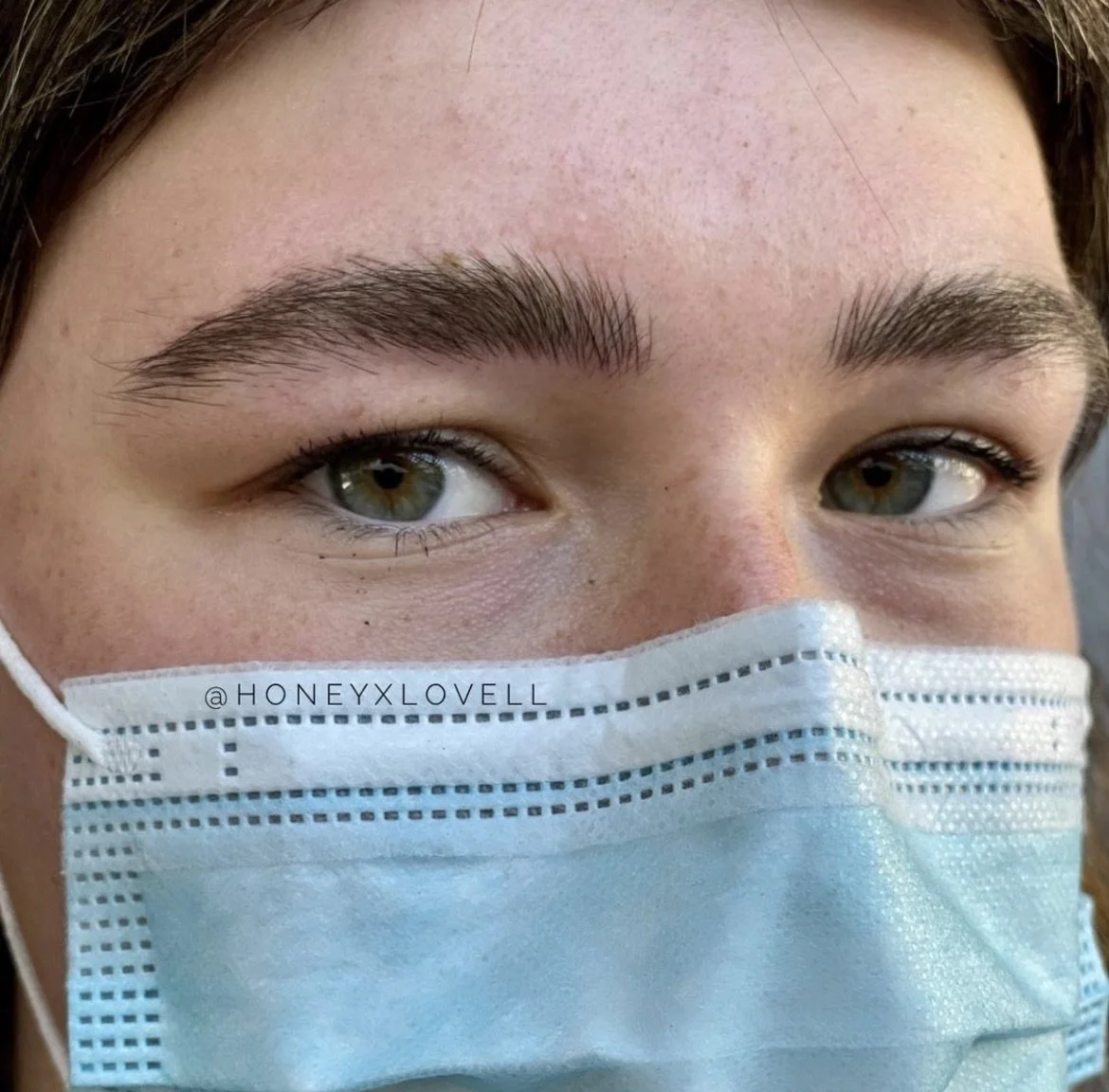 Close-up of a person wearing a surgical mask, showing their eyes, eyebrows, and part of their face.