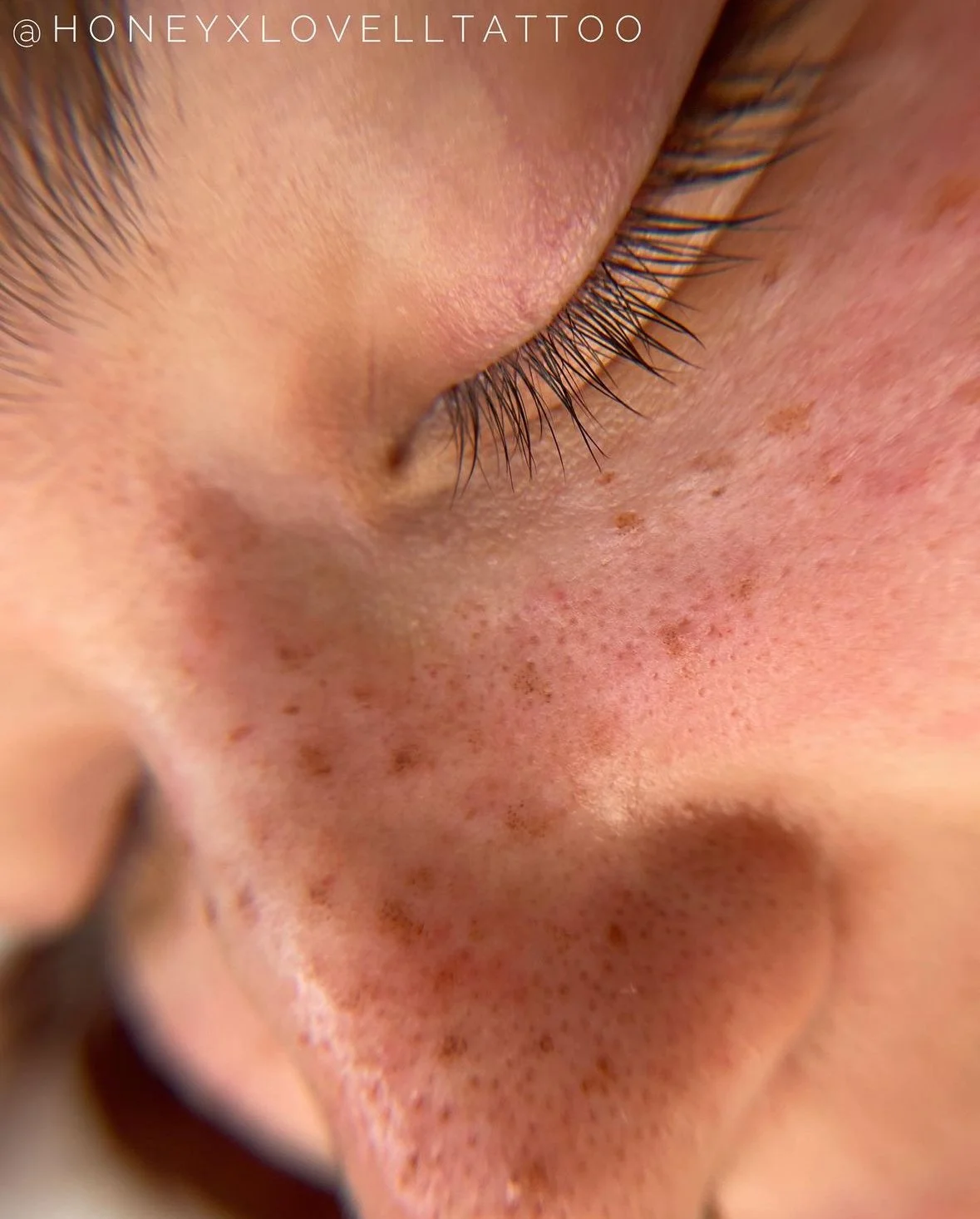 Close-up of a woman’s face showing her brown eyes, dark eyebrows, and freckles on her cheeks and nose.