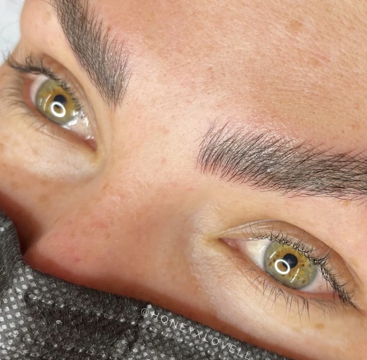 Close-up of a person's face showing hazel eyes, eyebrows, and part of the nose, with the person lying down on a textured surface.