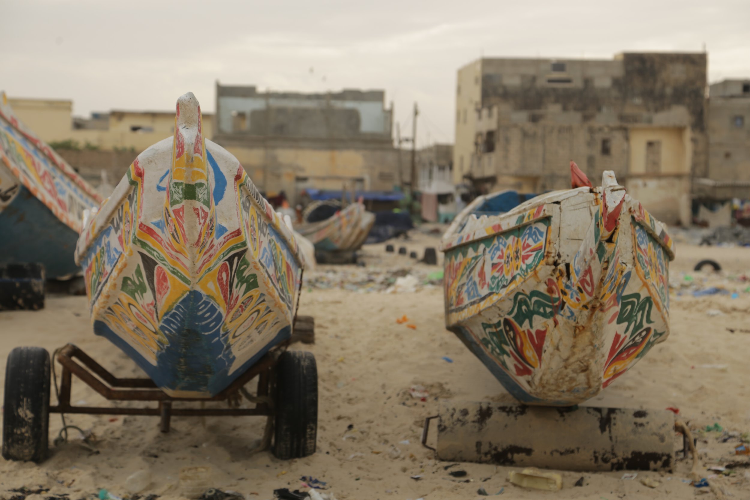 Dos barcos de pesca decorados con colores vibrantes en una playa con edificios en el fondo.