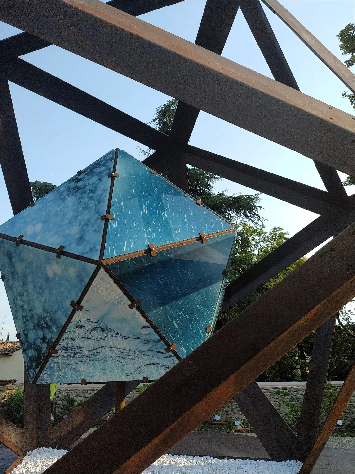 Estructura de madera con un cubo de vidrio con agua y burbujas, vista desde abajo hacia el cielo y árboles.