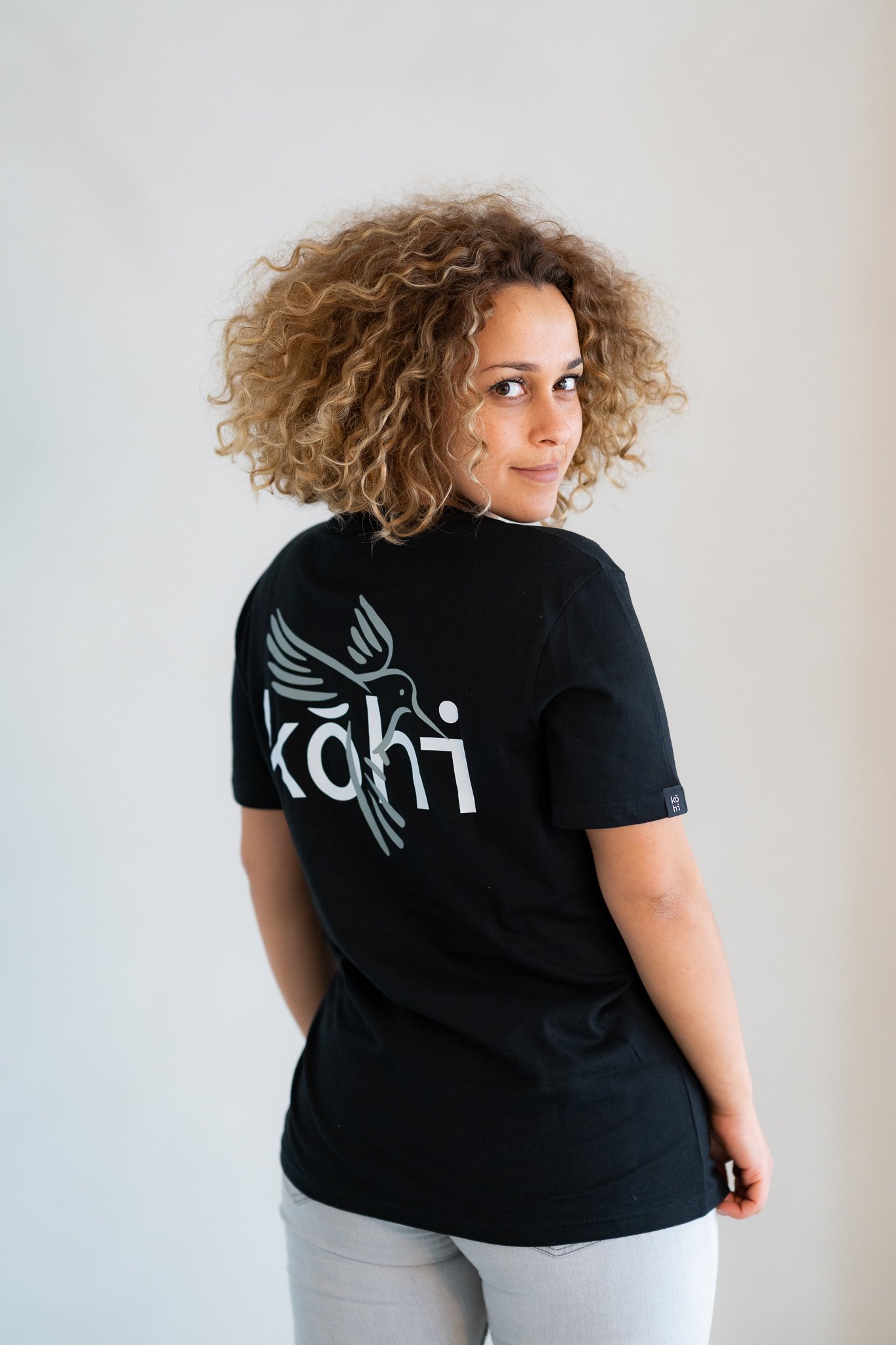 Weibliches Model trägt schwarzes Tshirt mit kohibri-Druck auf dem Rücken.