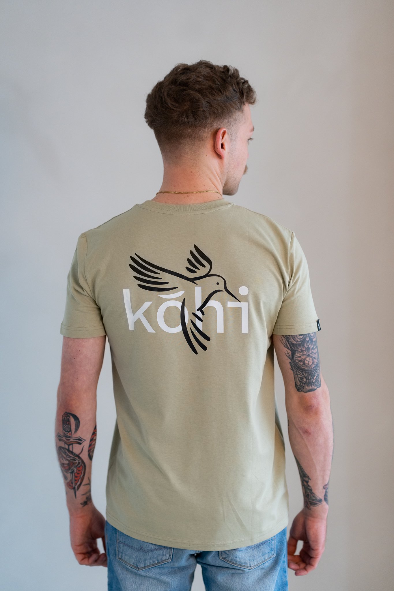 Männliches Model trägt salbeifarbenes Tshirt mit kohibri-Druck auf dem Rücken.