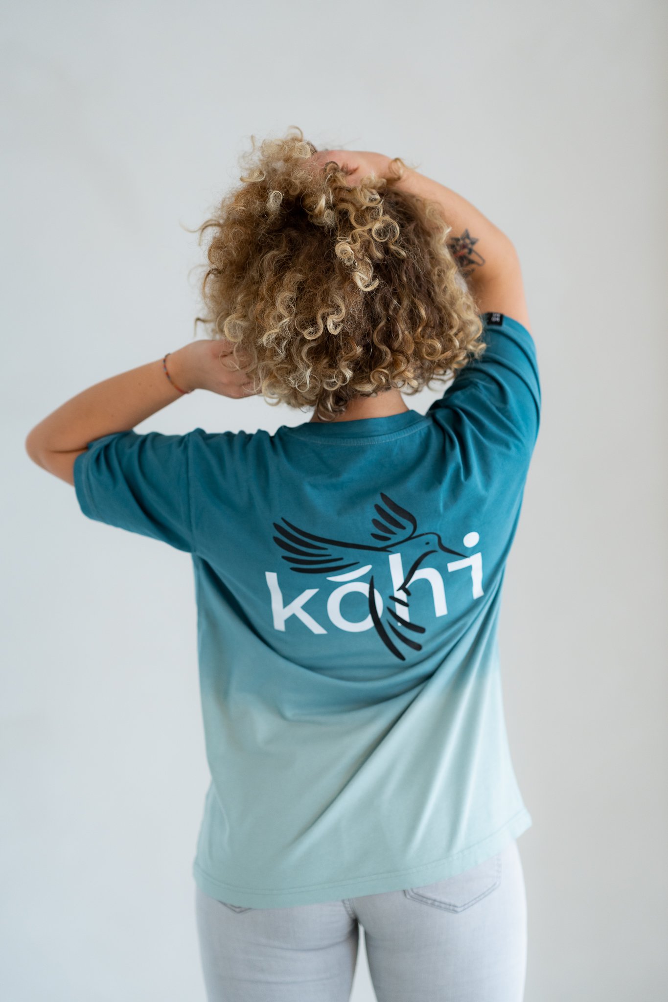 Weibliches Model trägt ocean-farbenes Tshirt mit einem kohibri-Druck auf dem Rücken.