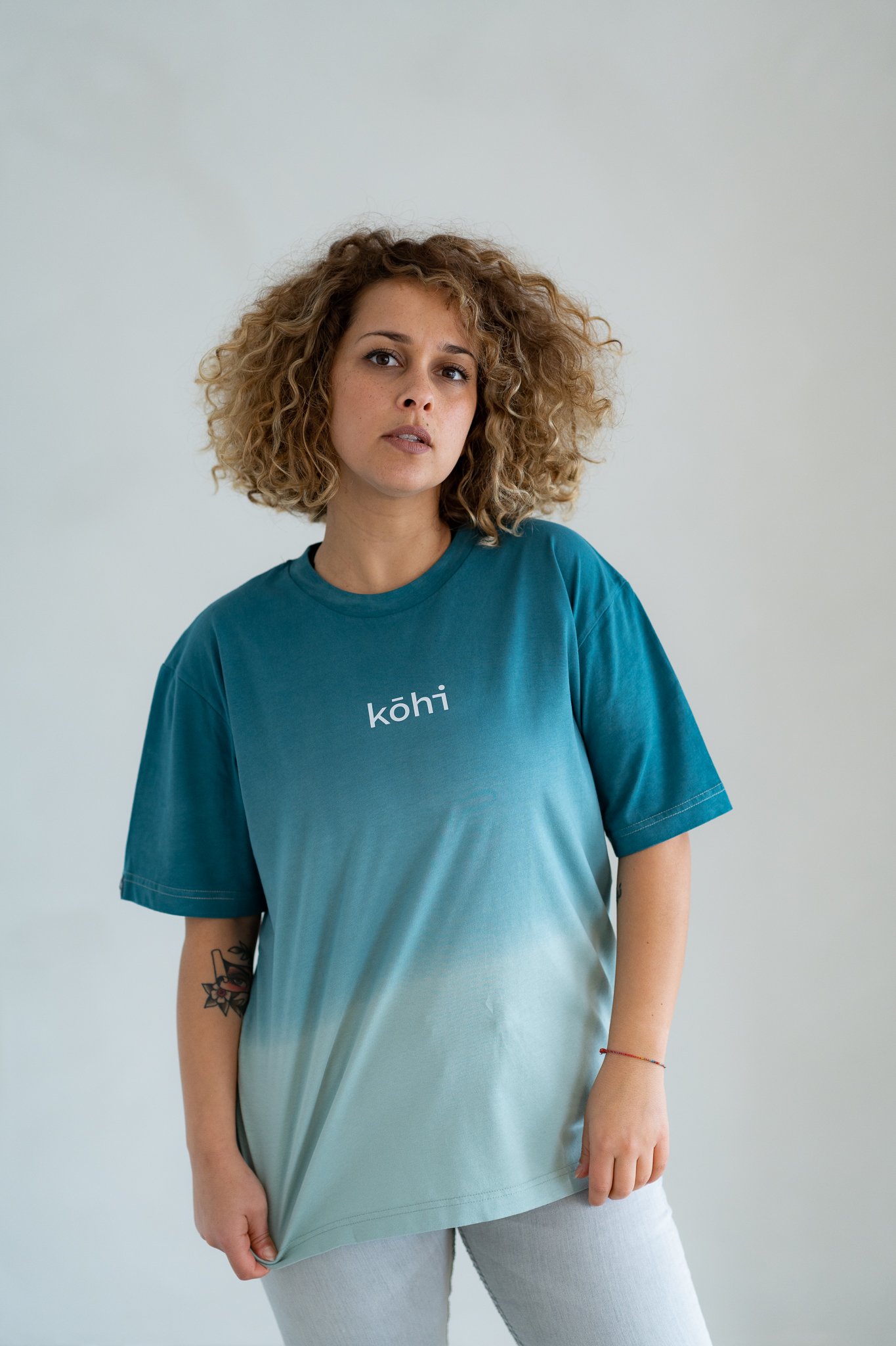 Weibliches Model trägt ocean-farbenes Tshirt mit einem kohi-Logo auf der Brust.