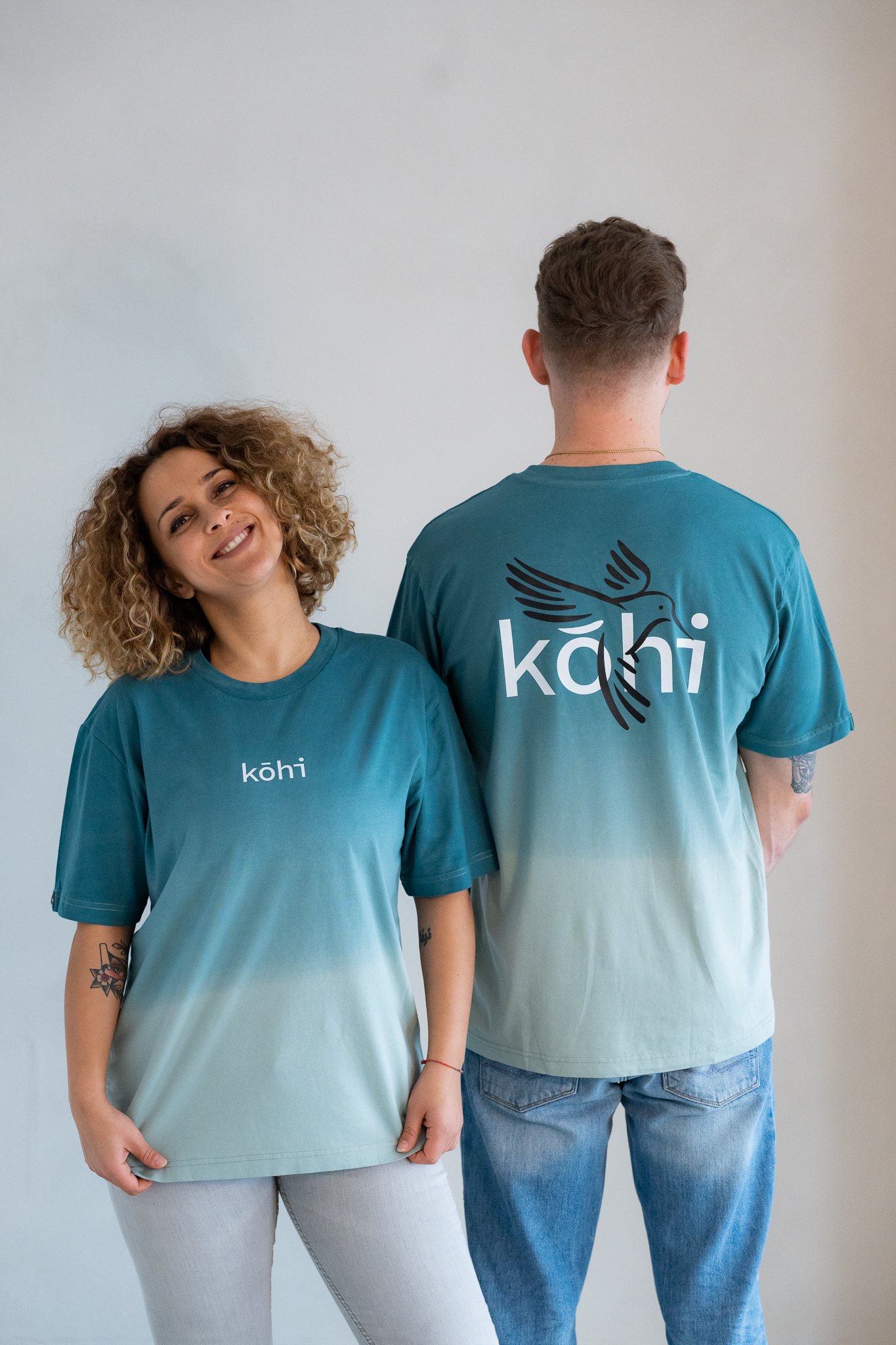 Paar trägt ocean-farbenes Tshirt mit einem kohibri-Druck auf dem Rücken und einem kohi-Logo auf der Brust.