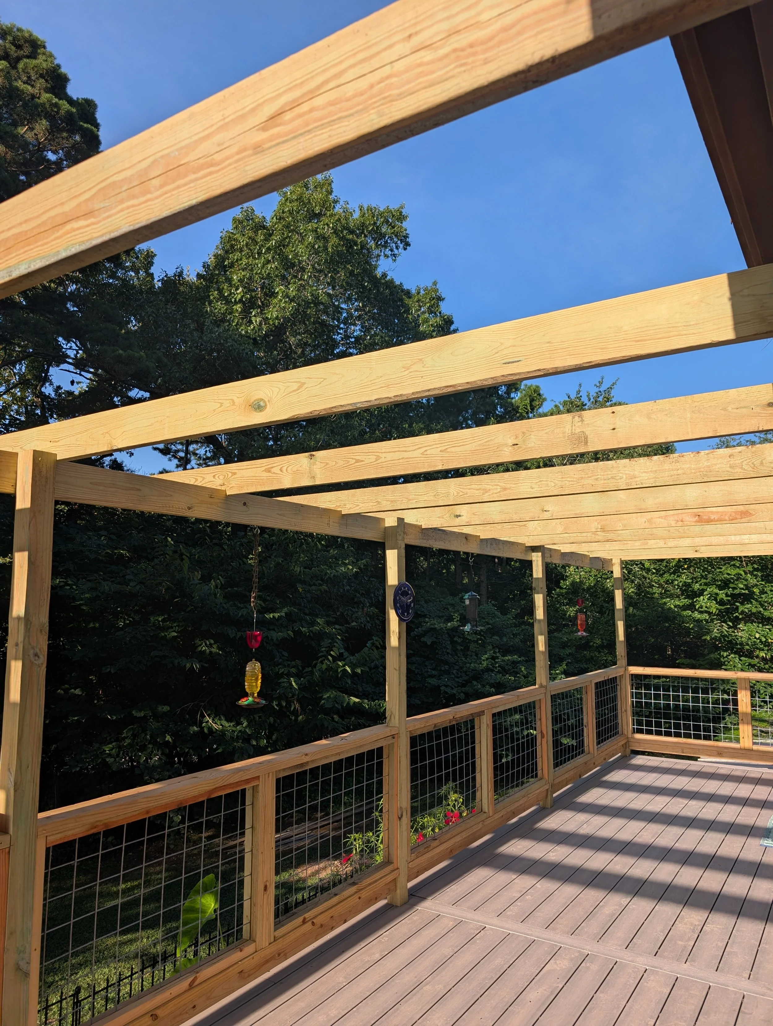 New wooden deck under construction with horizontal beams, surrounded by trees and a blue sky.