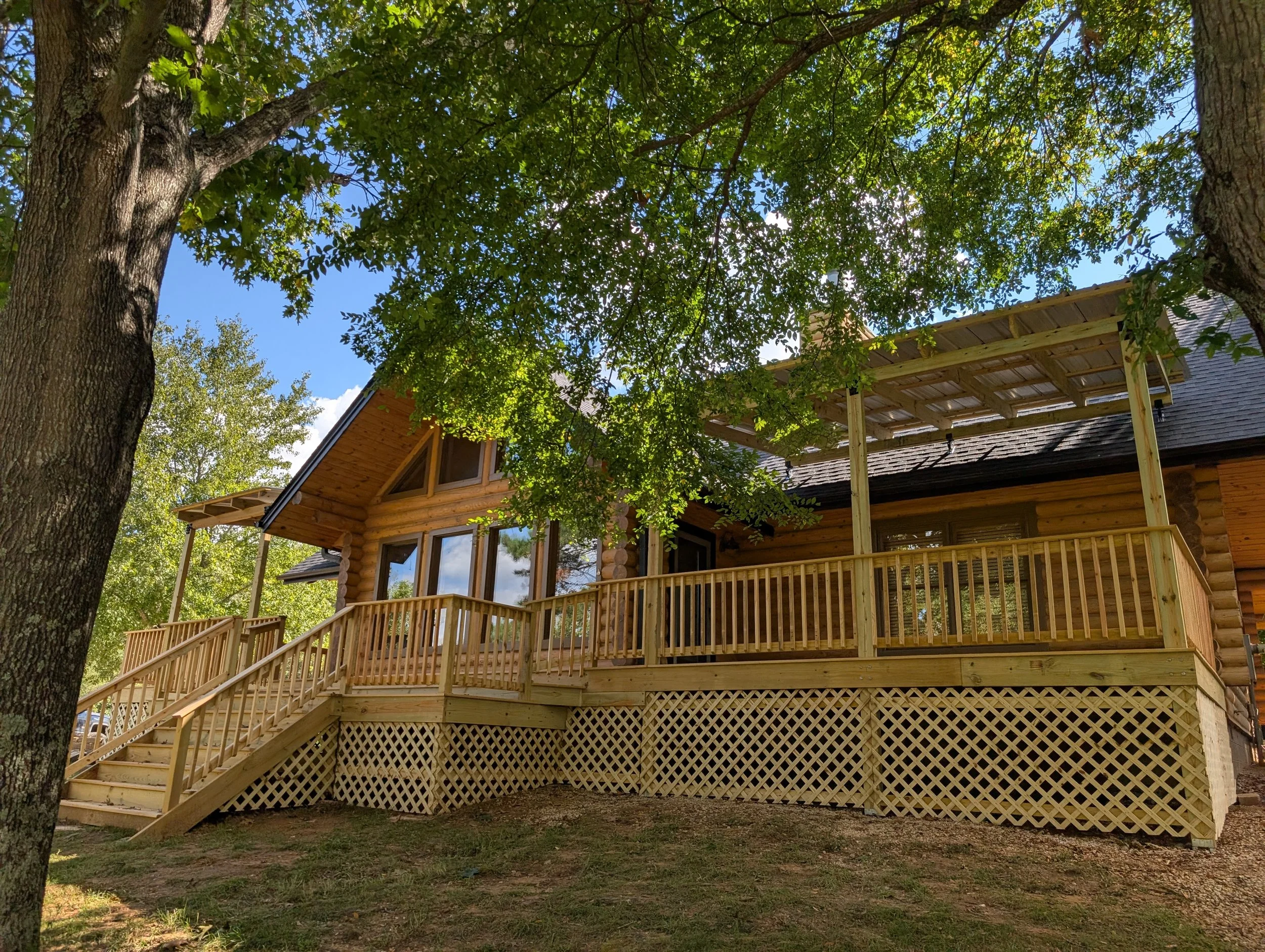 A wooden house with a large deck under green trees in a natural setting.