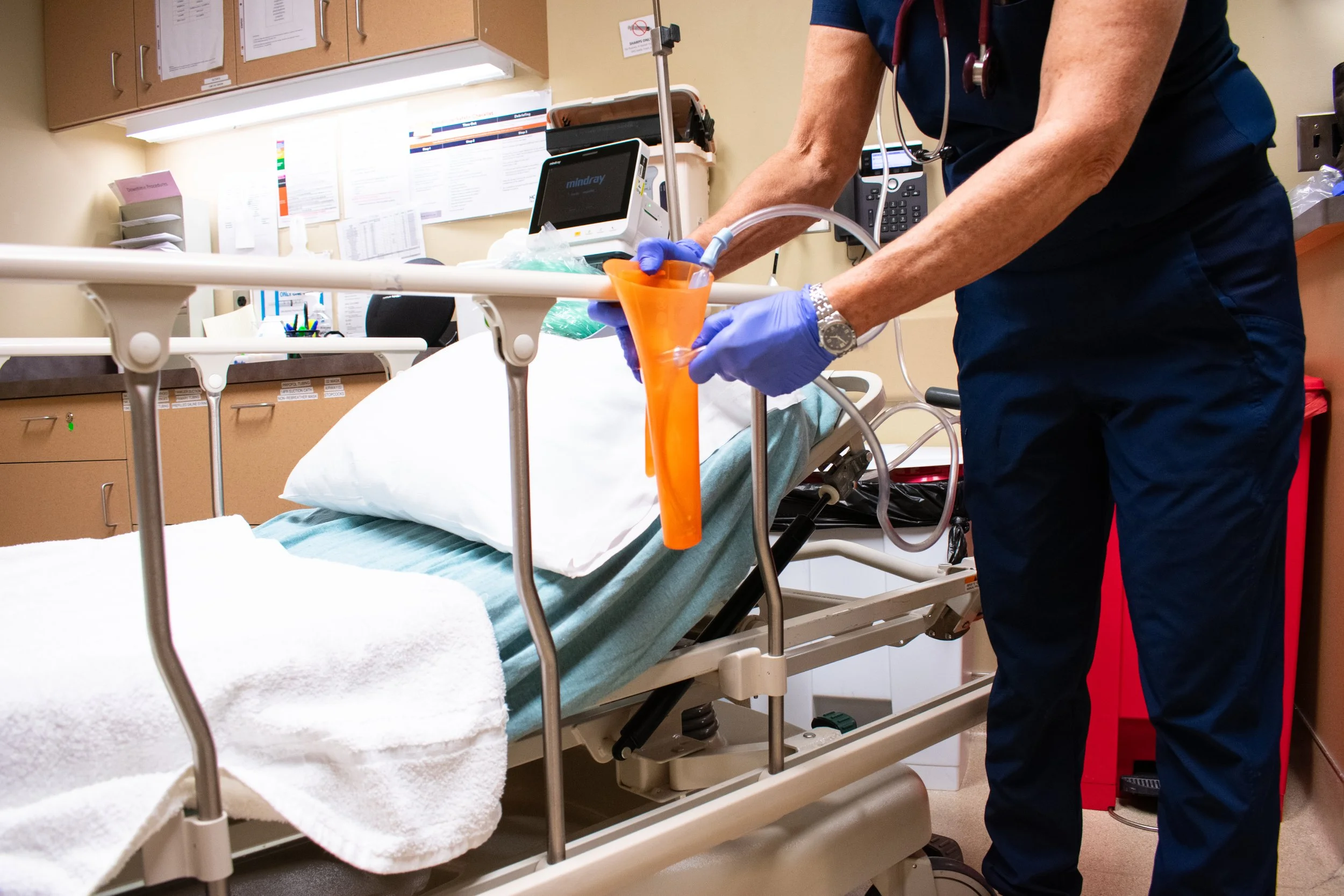 SuctionShield on Hospital Bed Rail with healthcare worker using the front aperture by pinching a little of the tubing into the Suctionshield