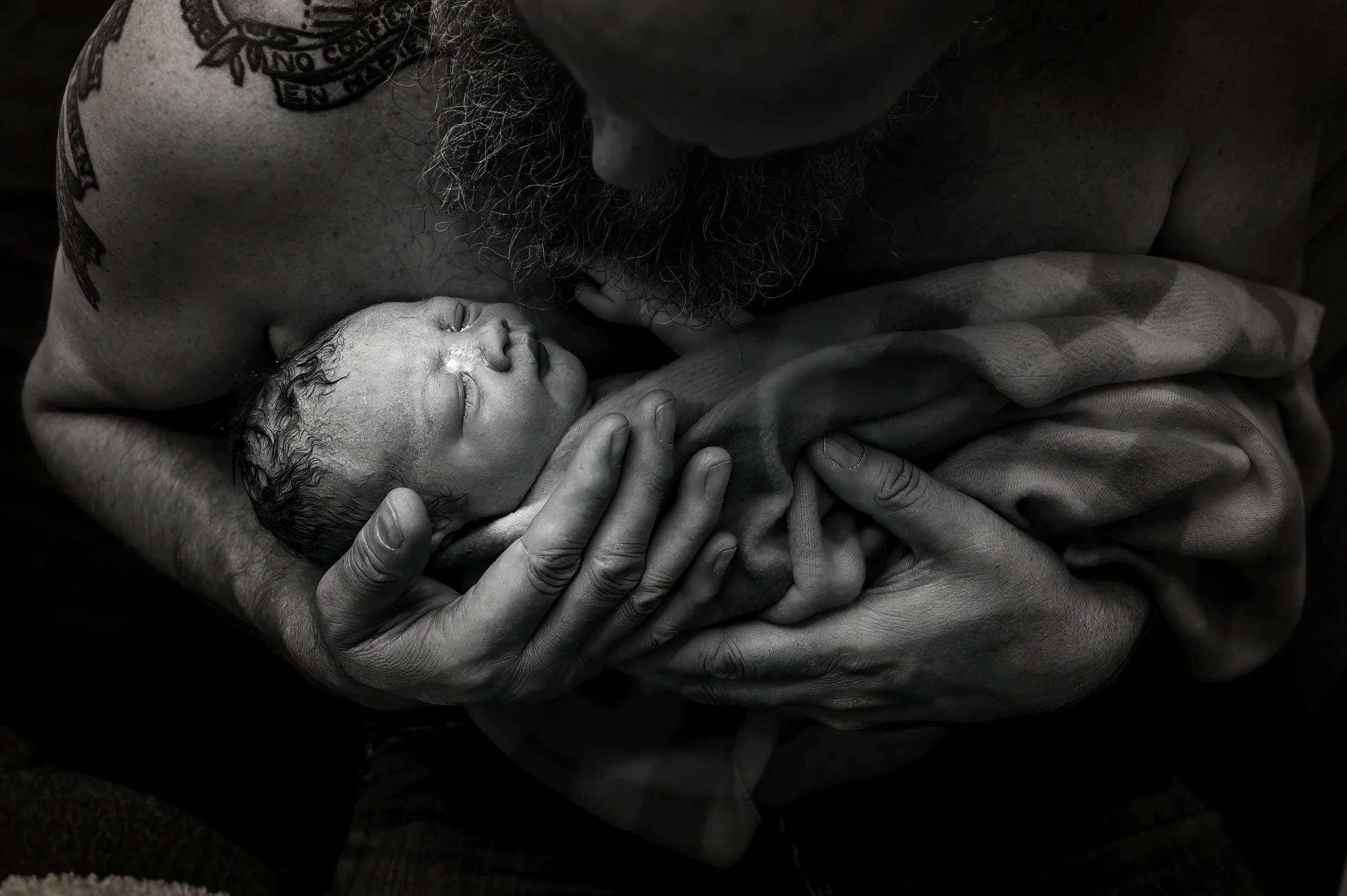 A man gently holding a newborn baby close to his chest, with their faces touching, in a tender moment of bonding.