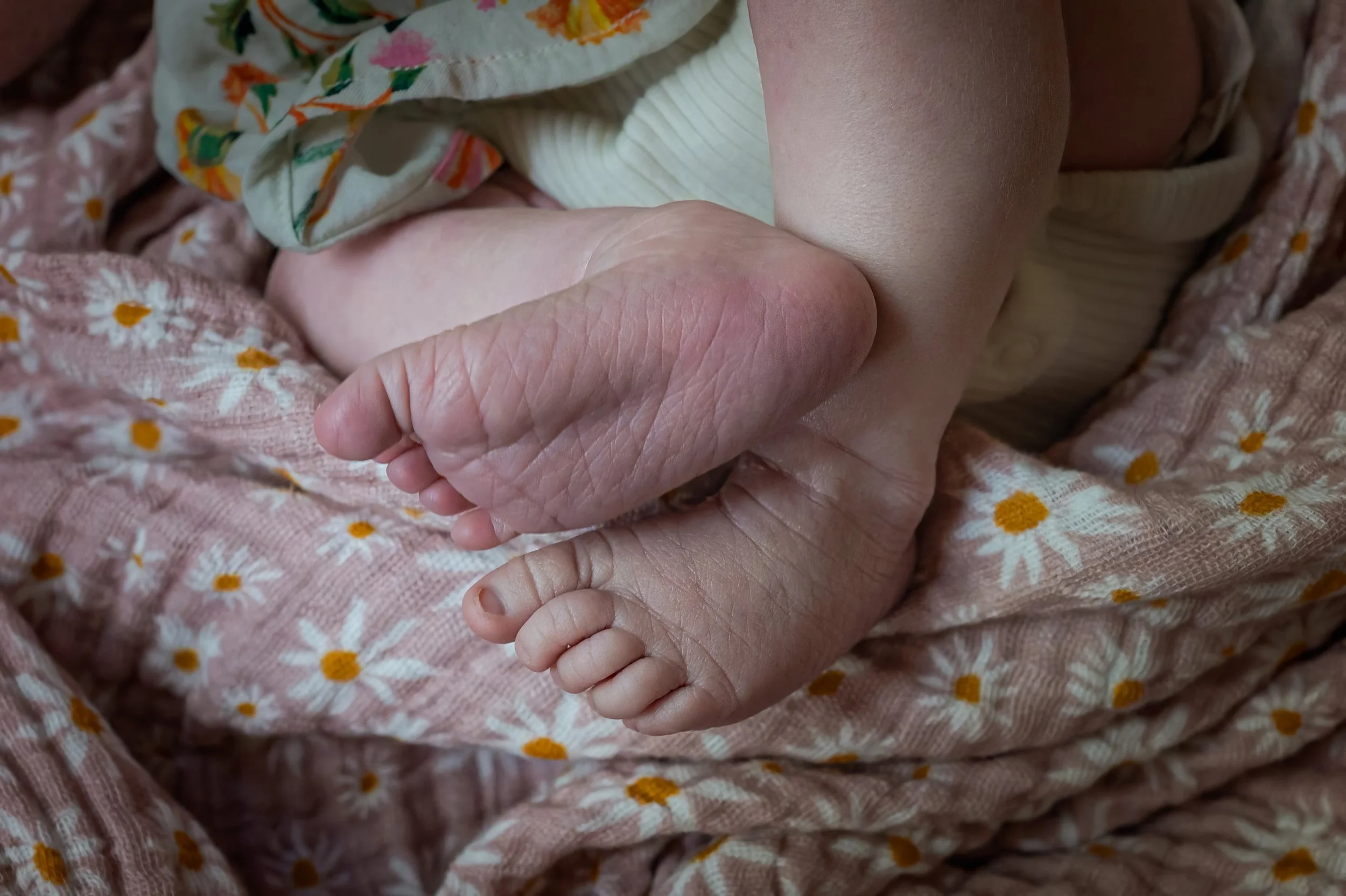 A close-up of a baby's tiny hand resting on an adult's hand, both lying on a pink blanket with white daisies and yellow centers.