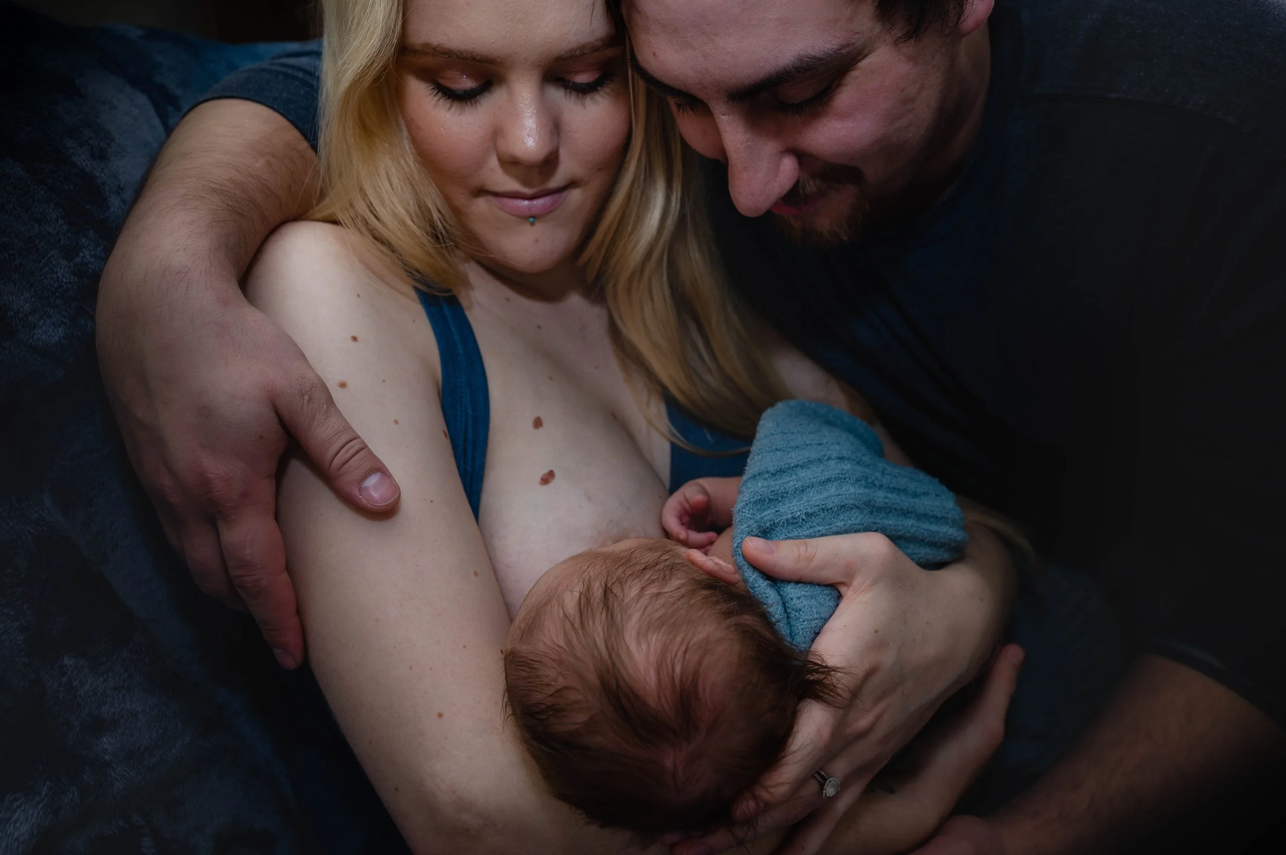 The homecoming sessions newborn photoshoot. mother and father holding their newborn who is swaddled in blue, staring at him and adoring him