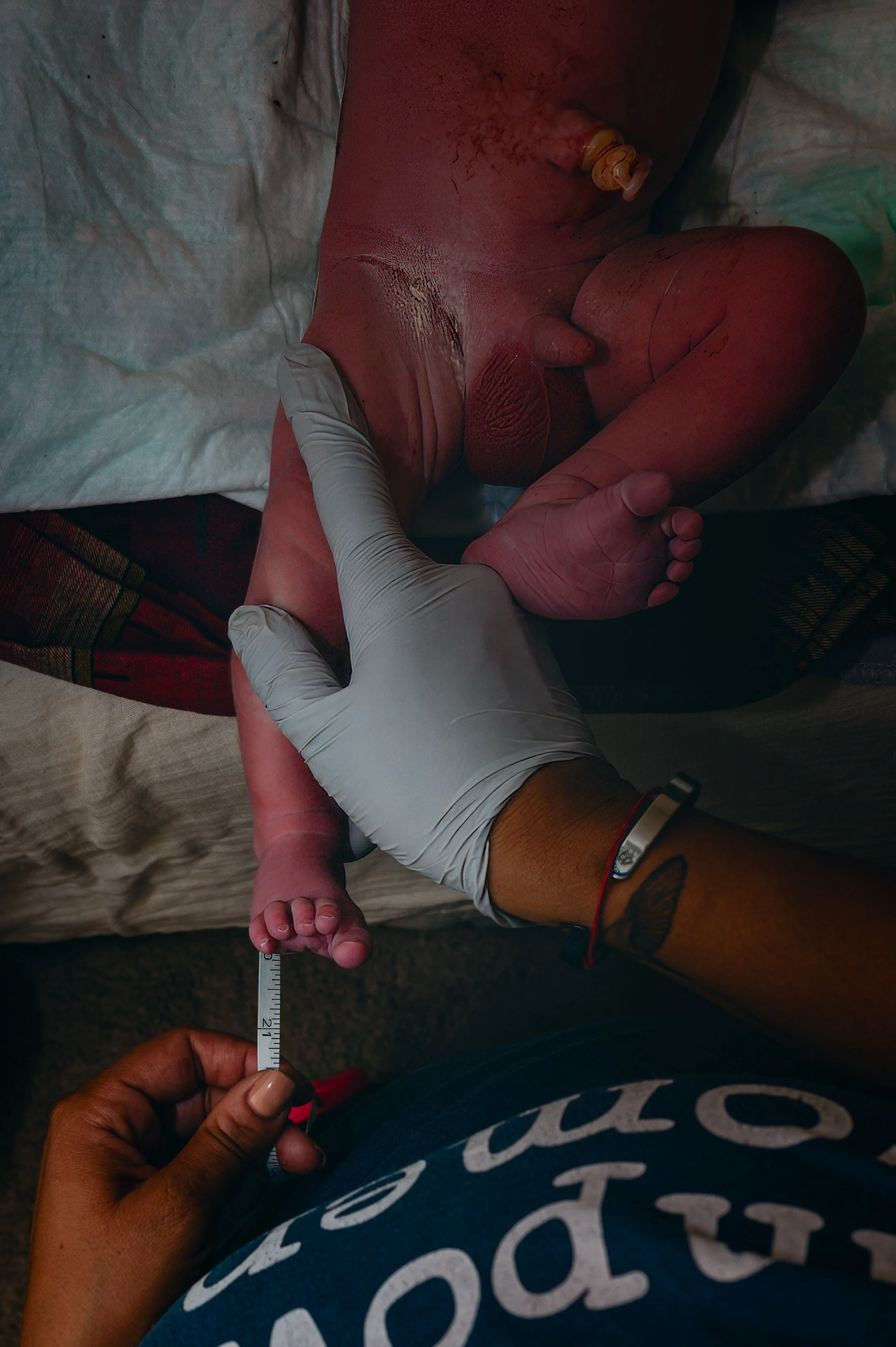 A newborn baby being measured with a ruler by a healthcare professional wearing gloves
