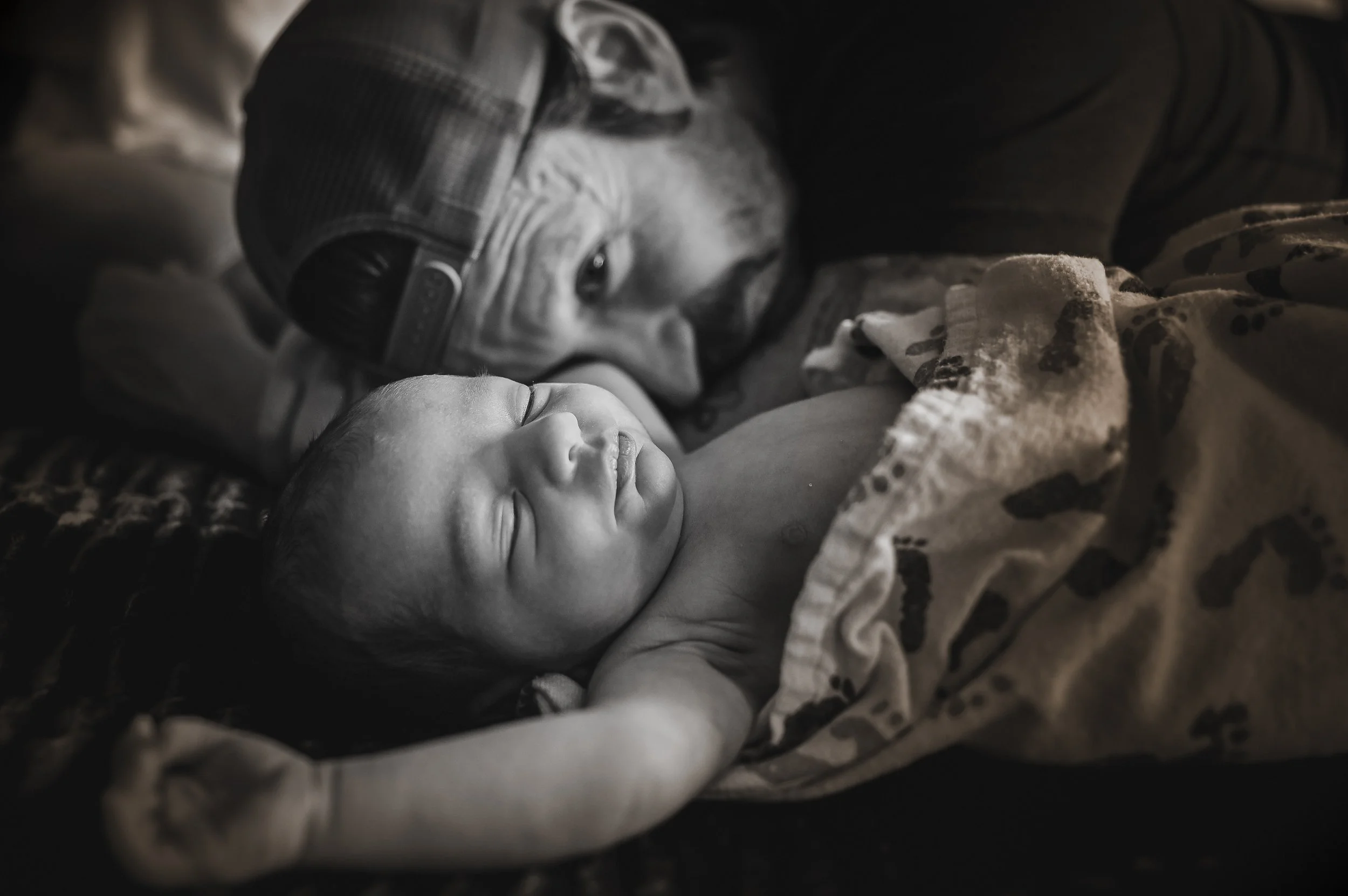 A man and a sleeping baby lying peacefully together, with the man resting his face next to the baby's head.