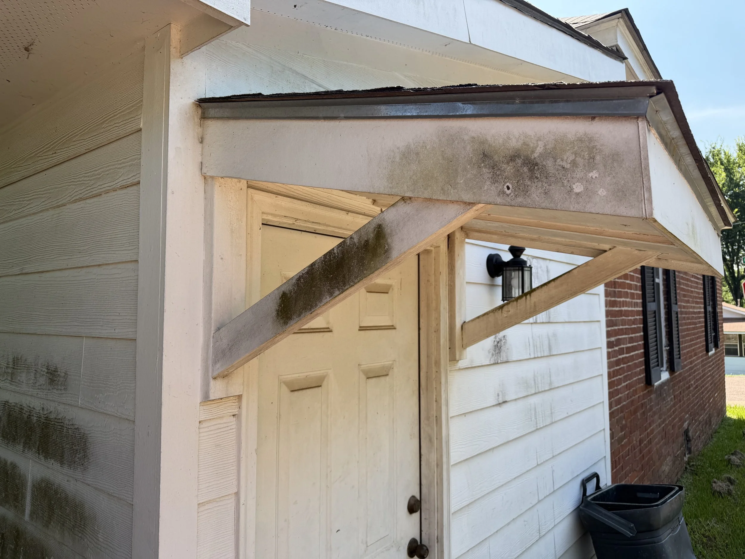 Side of a white garage exterior with porch overhang and exposed framing before exterior cleaning.