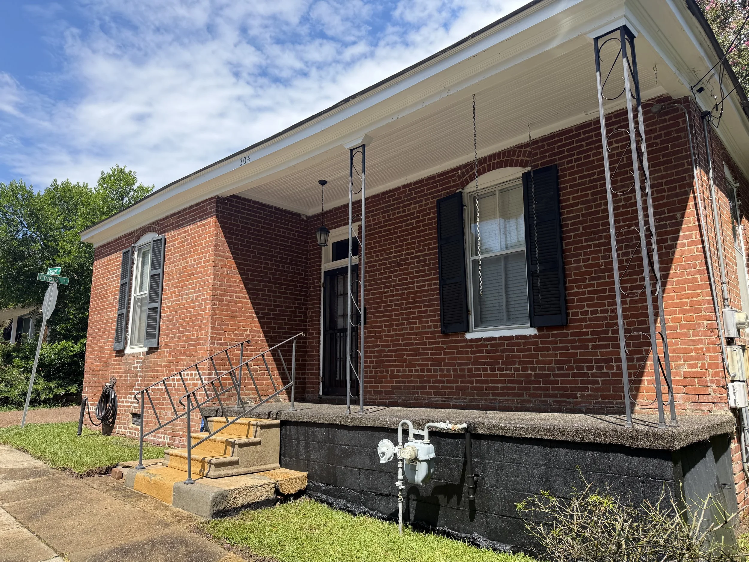 Front of a brick house with black shutters and a covered porch, with steps leading up to the entrance, and a street sign at the corner that reads 'Castell Phipps Ave'.