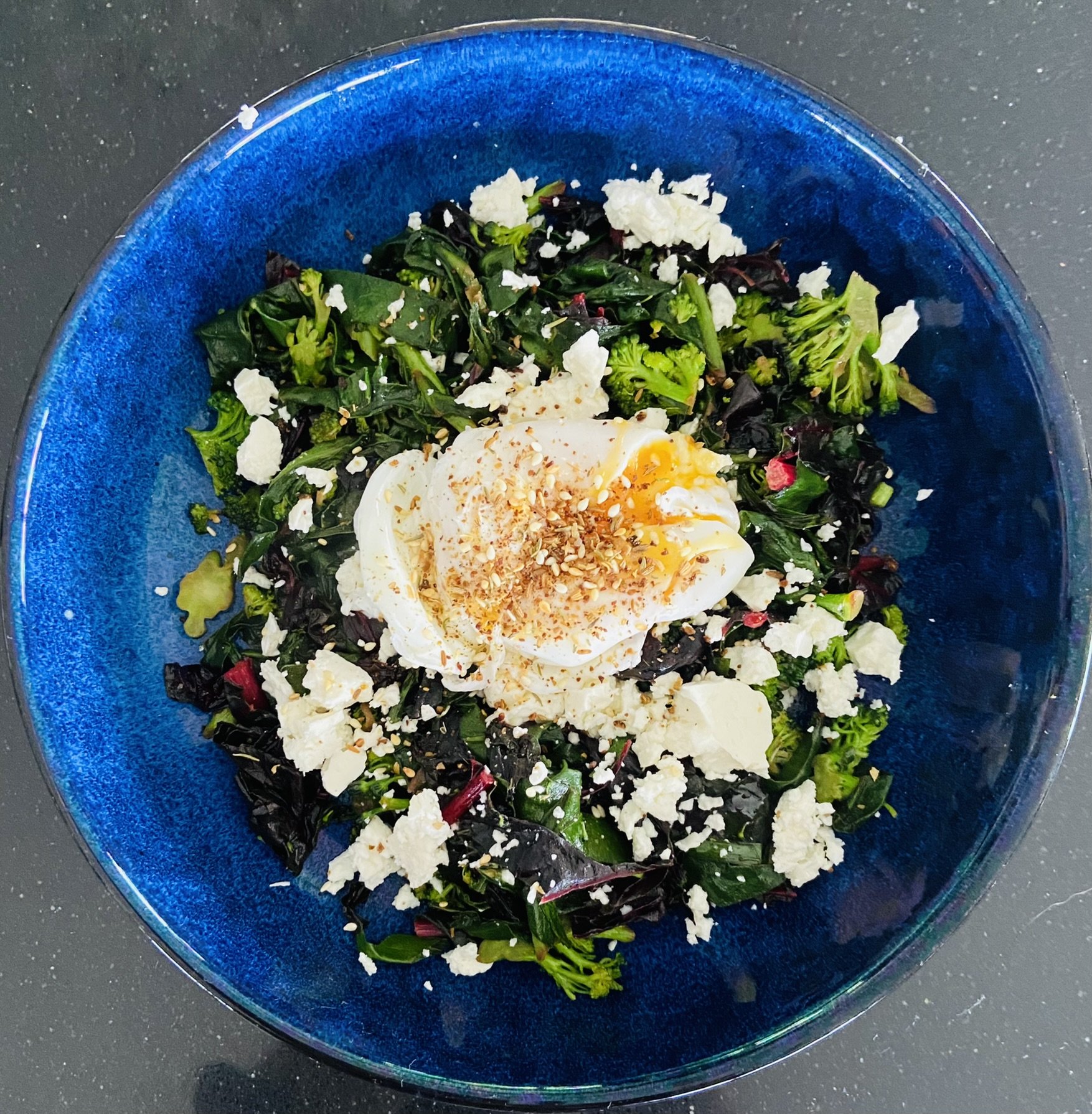 Perfect poached egg with buttery green vegetables served with Za'ztar and goat feta