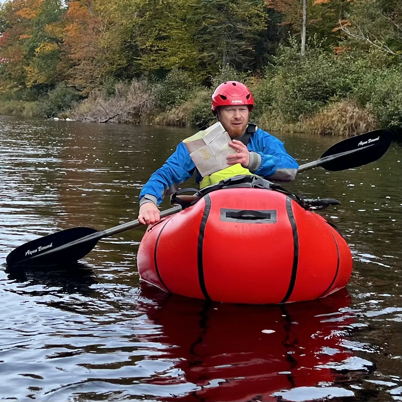 Person looks at map while sitting in a red packraft