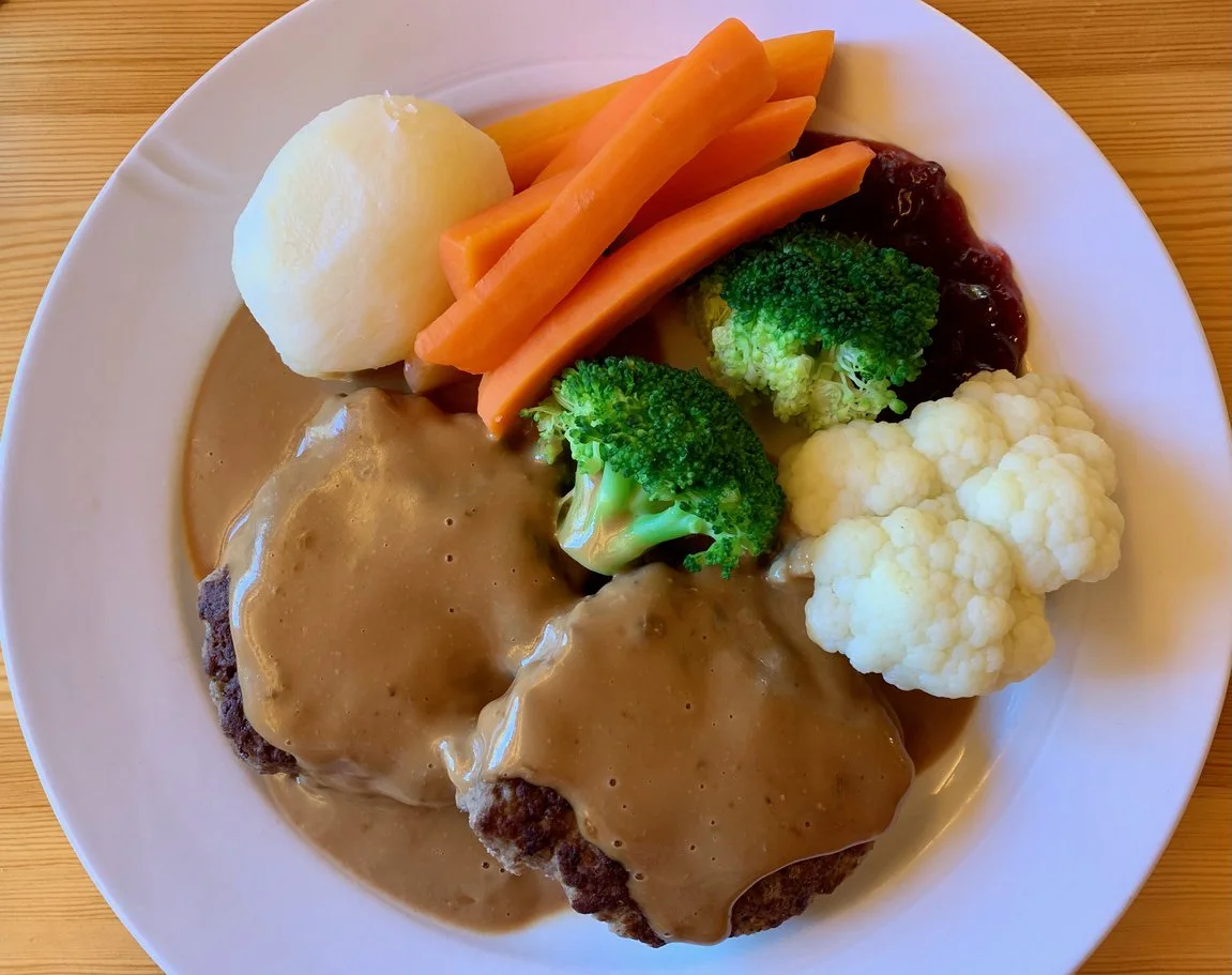 kjøttkaker, meat patties in a brown cheese sauce, with carrots, broccoli, and a potato, on a plate