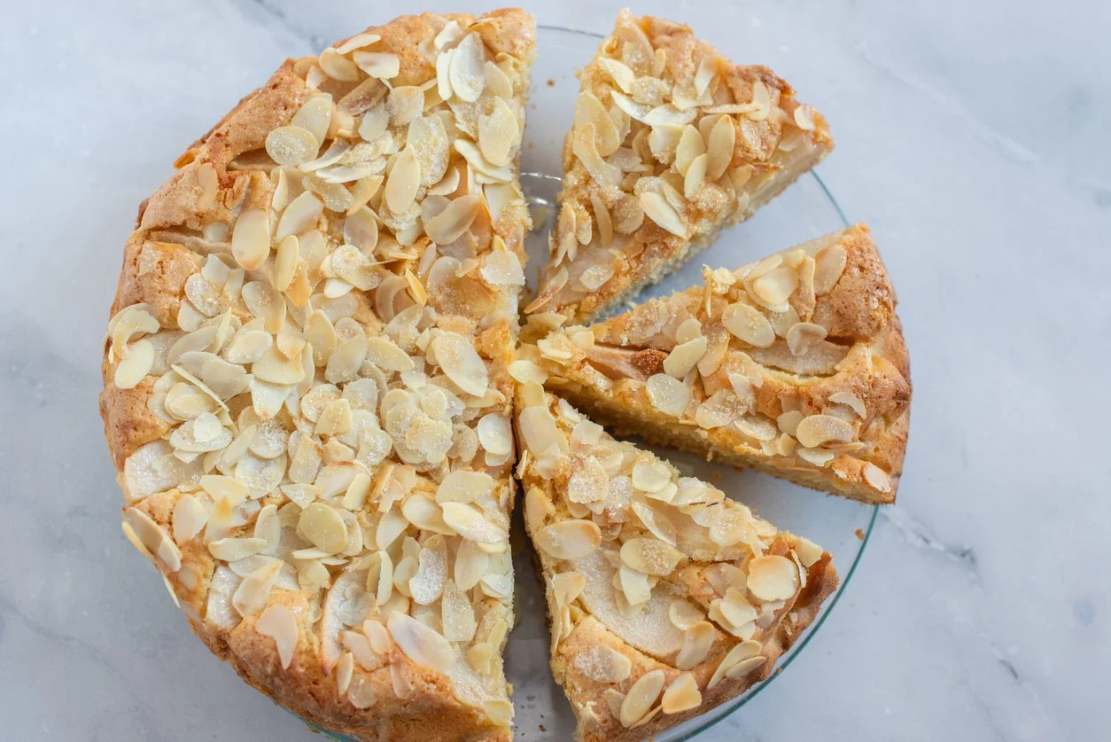 a thin cake covered in toasted sliced almonds, cut into wedges, on a clear plate