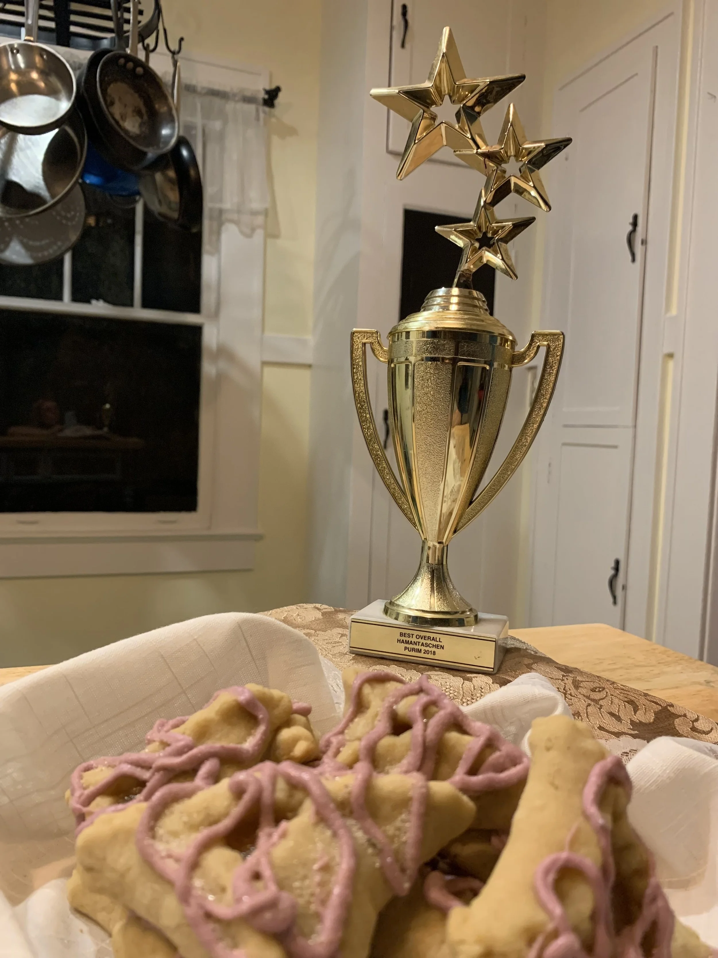 hamantaschen pastries with lavender colored icing squiggle over the top, plus a first place trophy