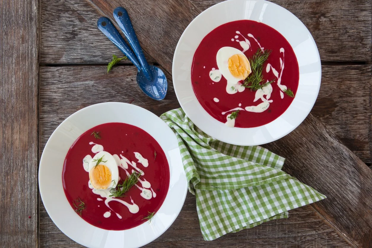 Two white bowls with creamy borscht topped with swirls of sour cream and half a boiled egg