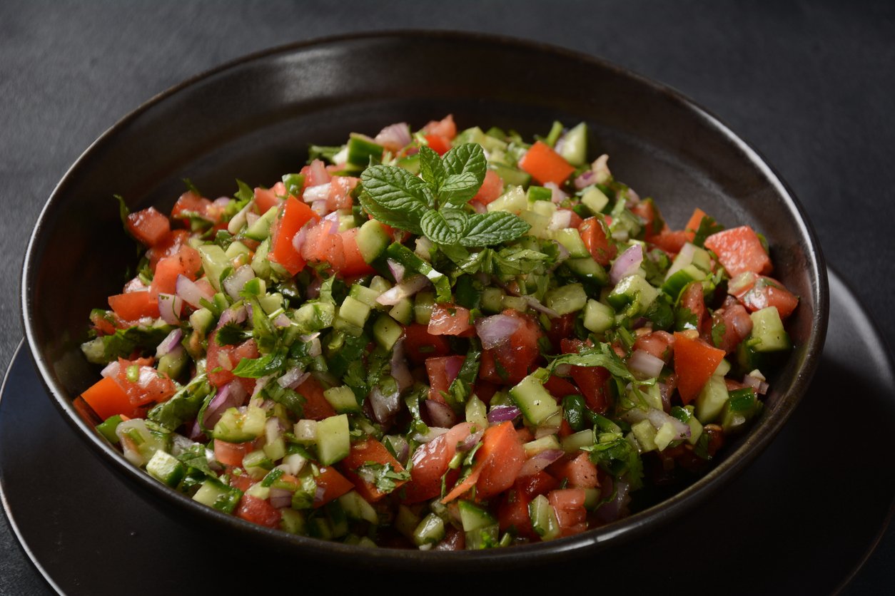 a black bowl filled with chopped tomatoes, cucumbers, and herbs