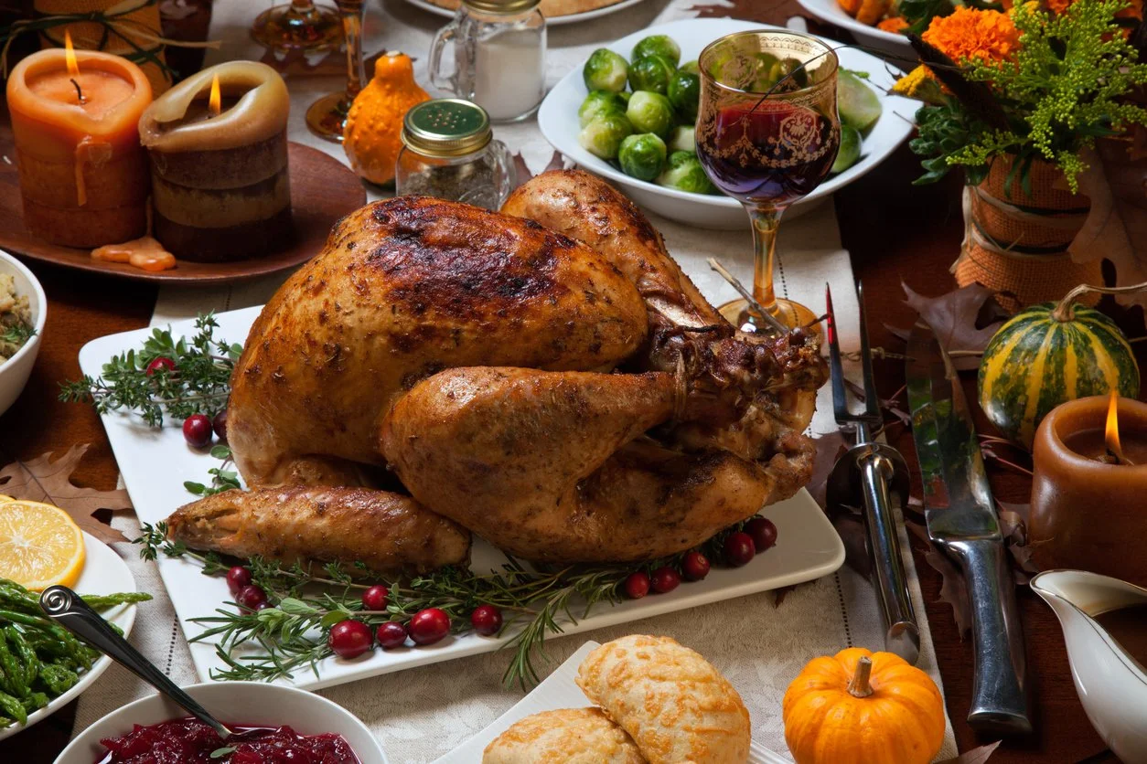 a platter with a roasted turkey on a table, with bowls of vegetables and autumn decor