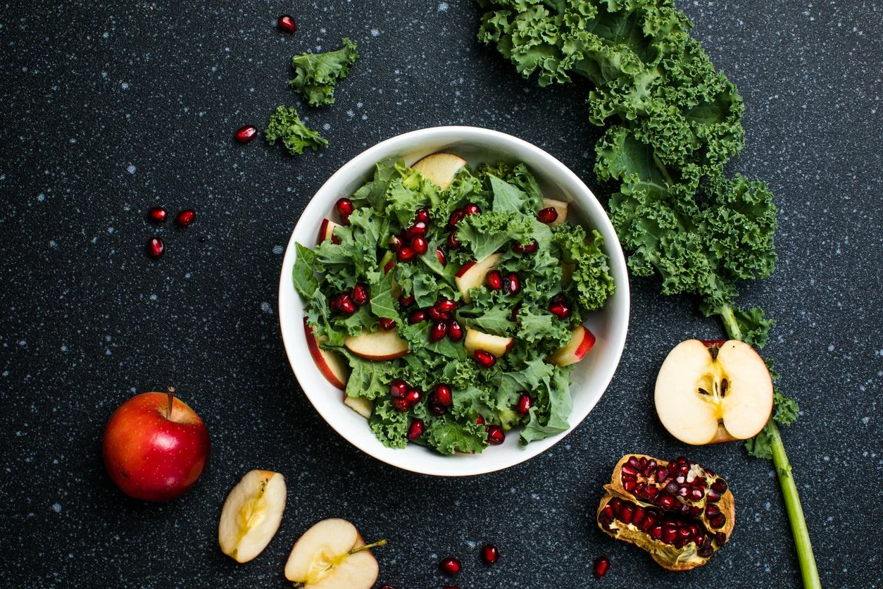 kale salad in a bowl with pomegranate and apples