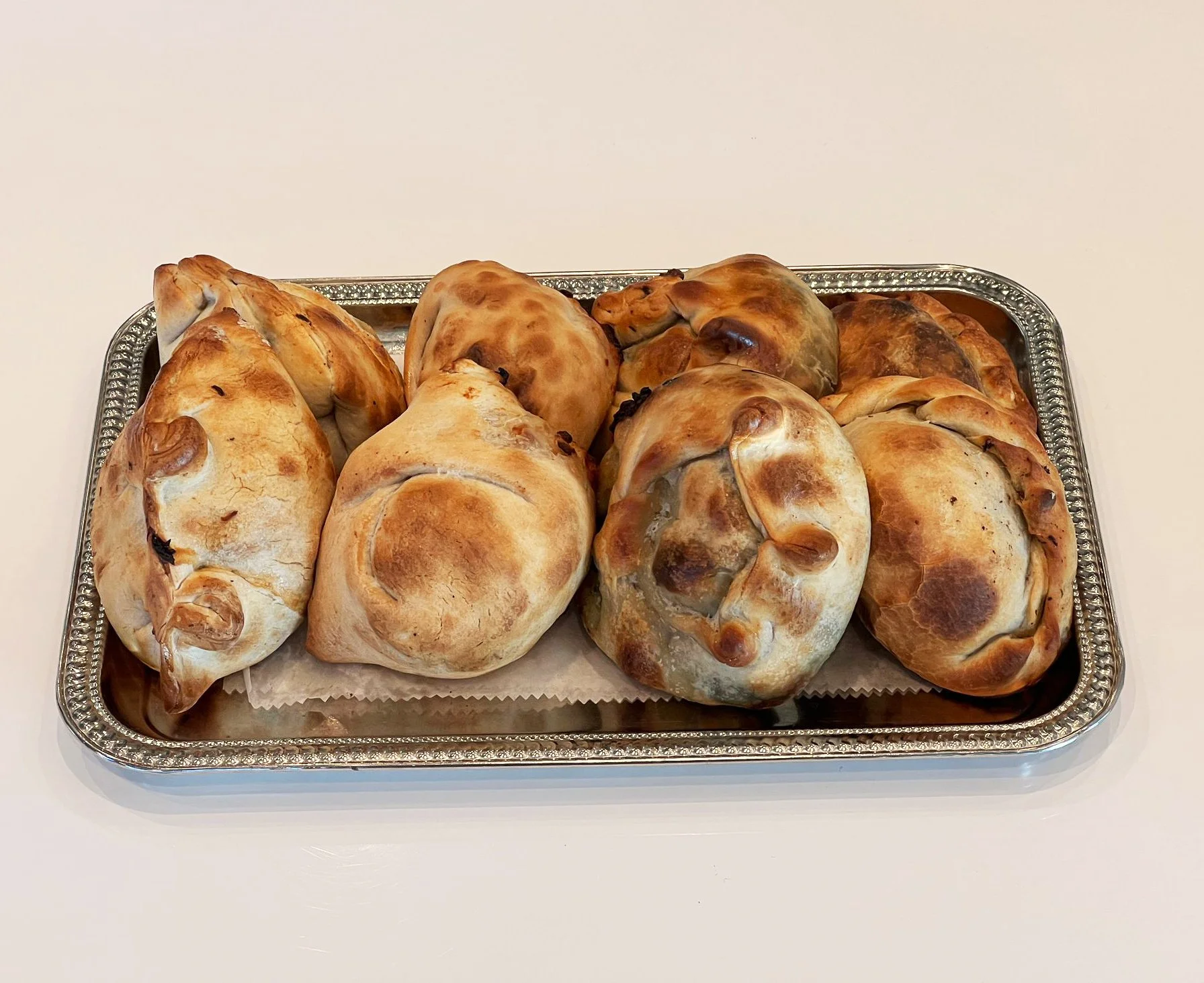 Assorted baked bagels on a decorative silver tray with parchment paper.