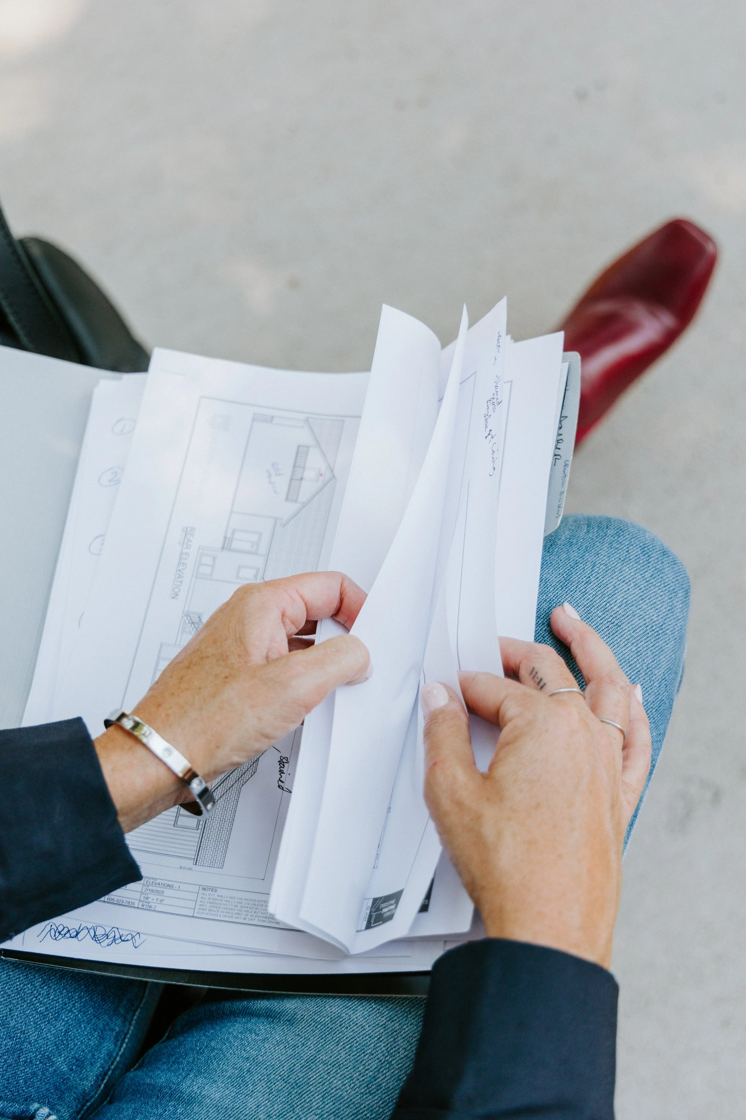 Chelsea Veurink Interior Design holding blueprints or architectural plans, showing floor plans and sketches, while sitting outdoors.