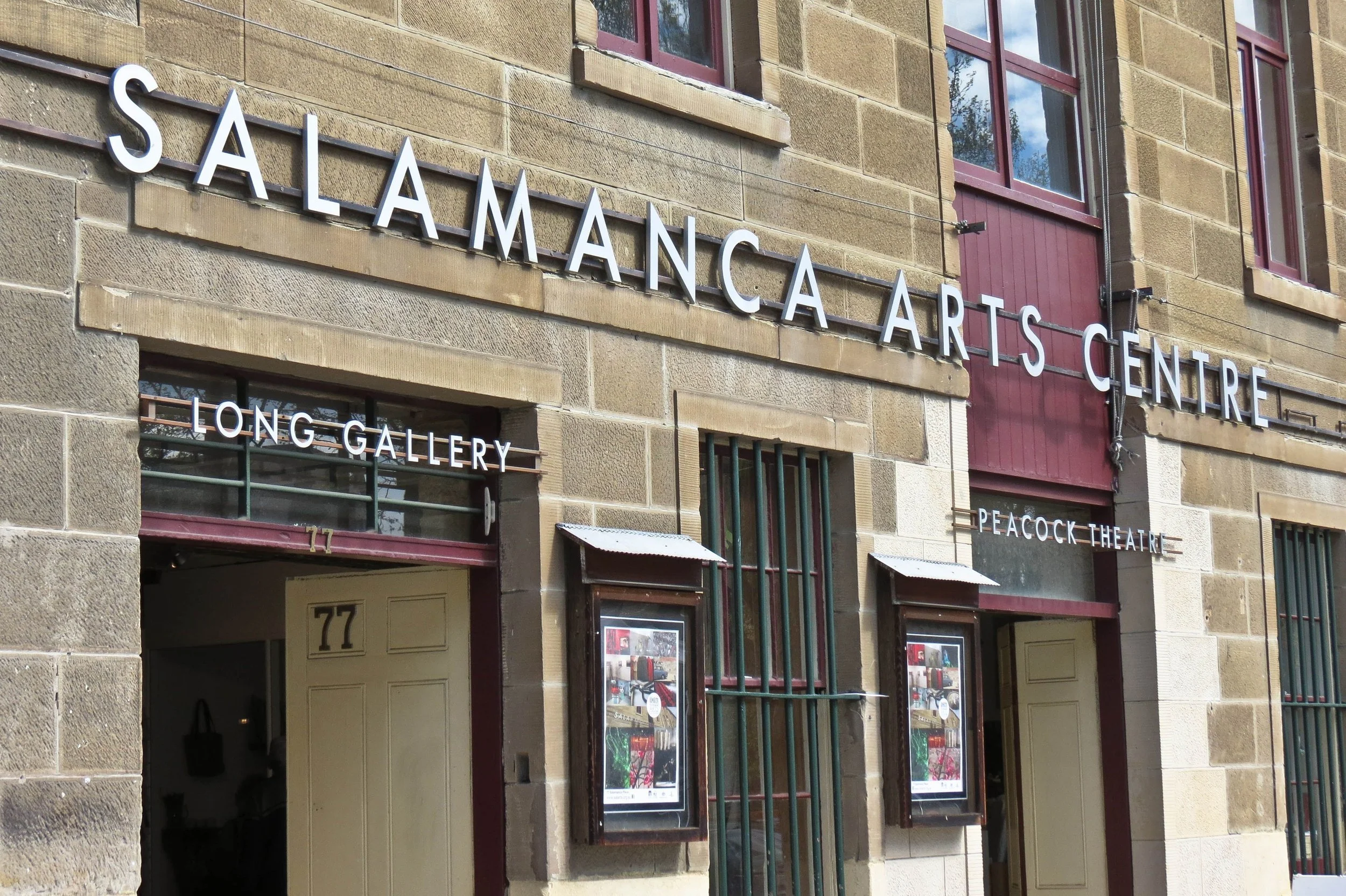 Exterior of the Salamanza Arts Centre building, showing signage for Long Gallery and Peacock Theatre, with a brick facade and framed posters outside.
