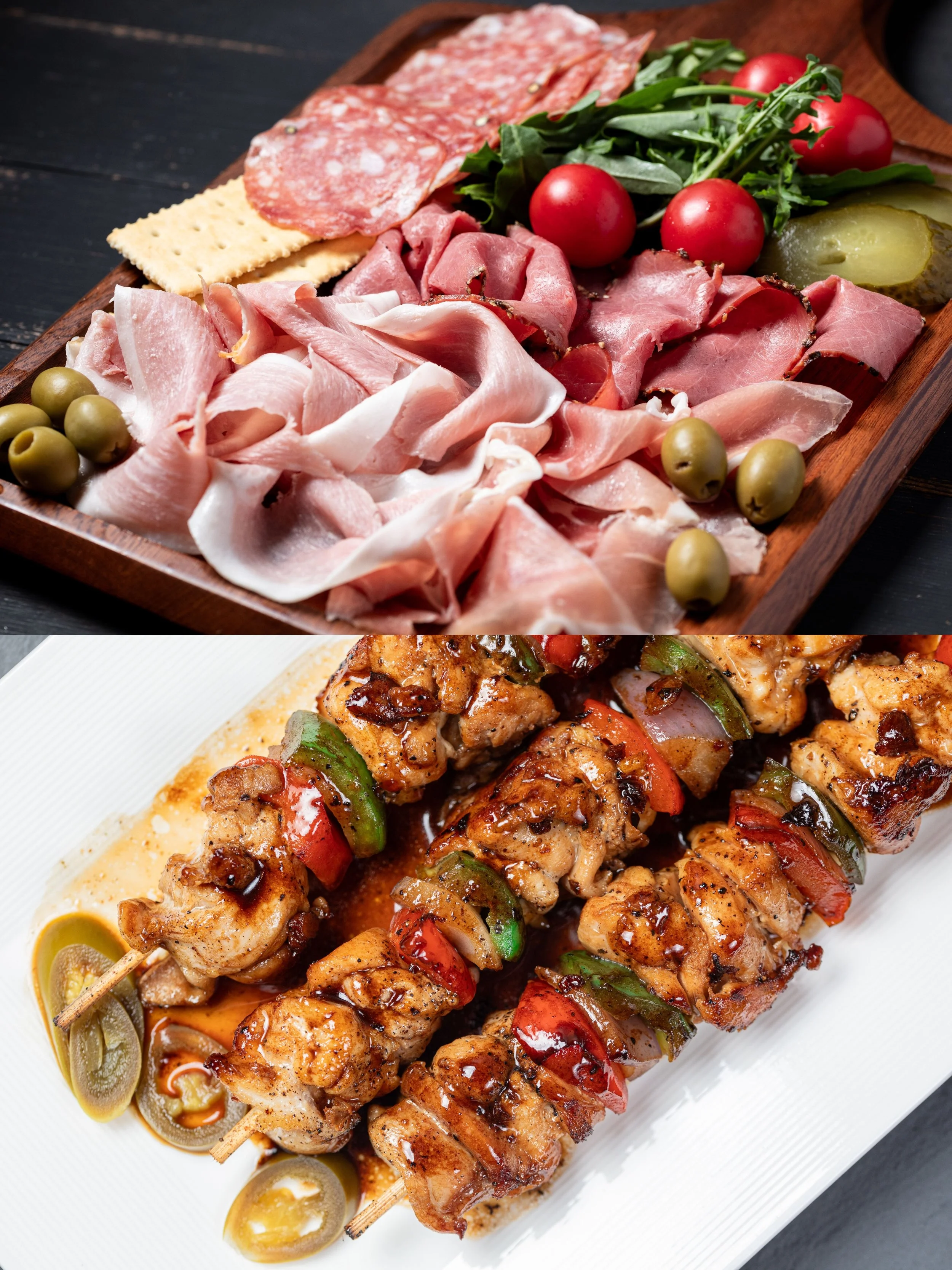 A charcuterie board with assorted sliced meats, cherry tomatoes, pickles, green olives, and crackers, alongside a plate of grilled chicken skewers with peppers and a dipping sauce.