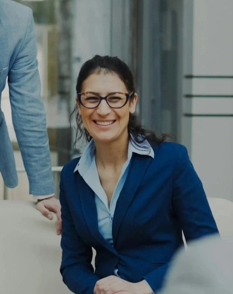 Woman smiling, wearing glasses, dark hair, in a professional setting.