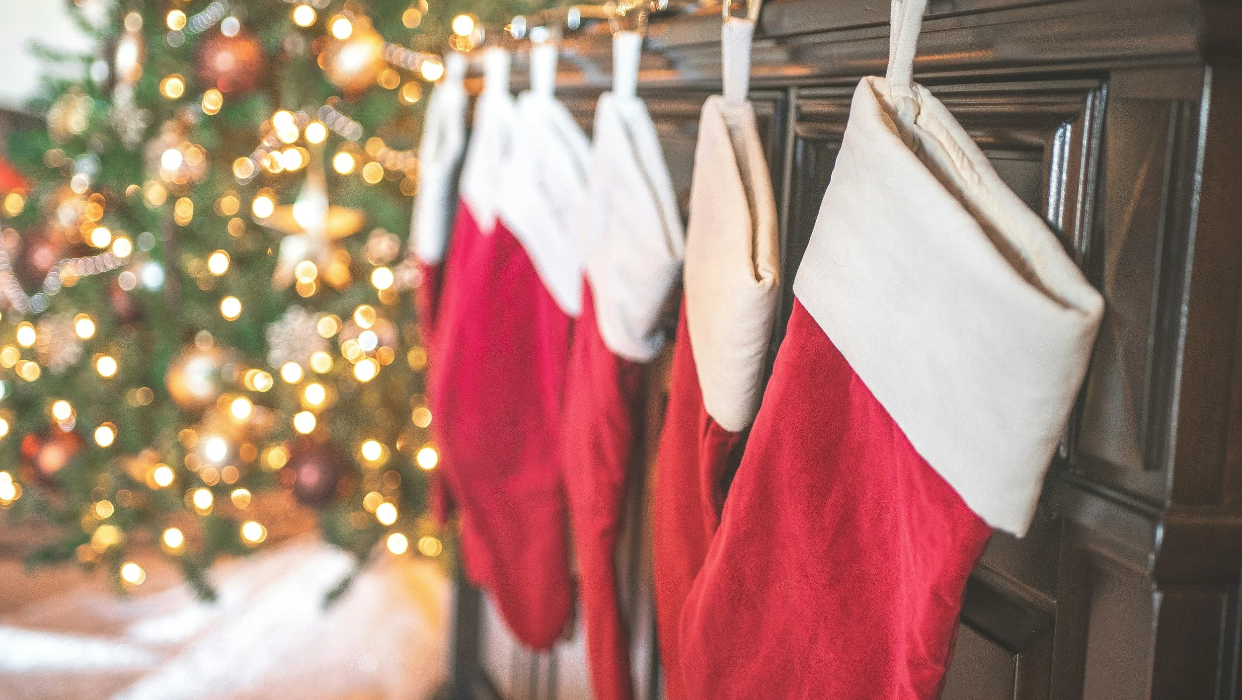 red and white stockings hanging on a brown cabinet with a lit Christmas tree in the background