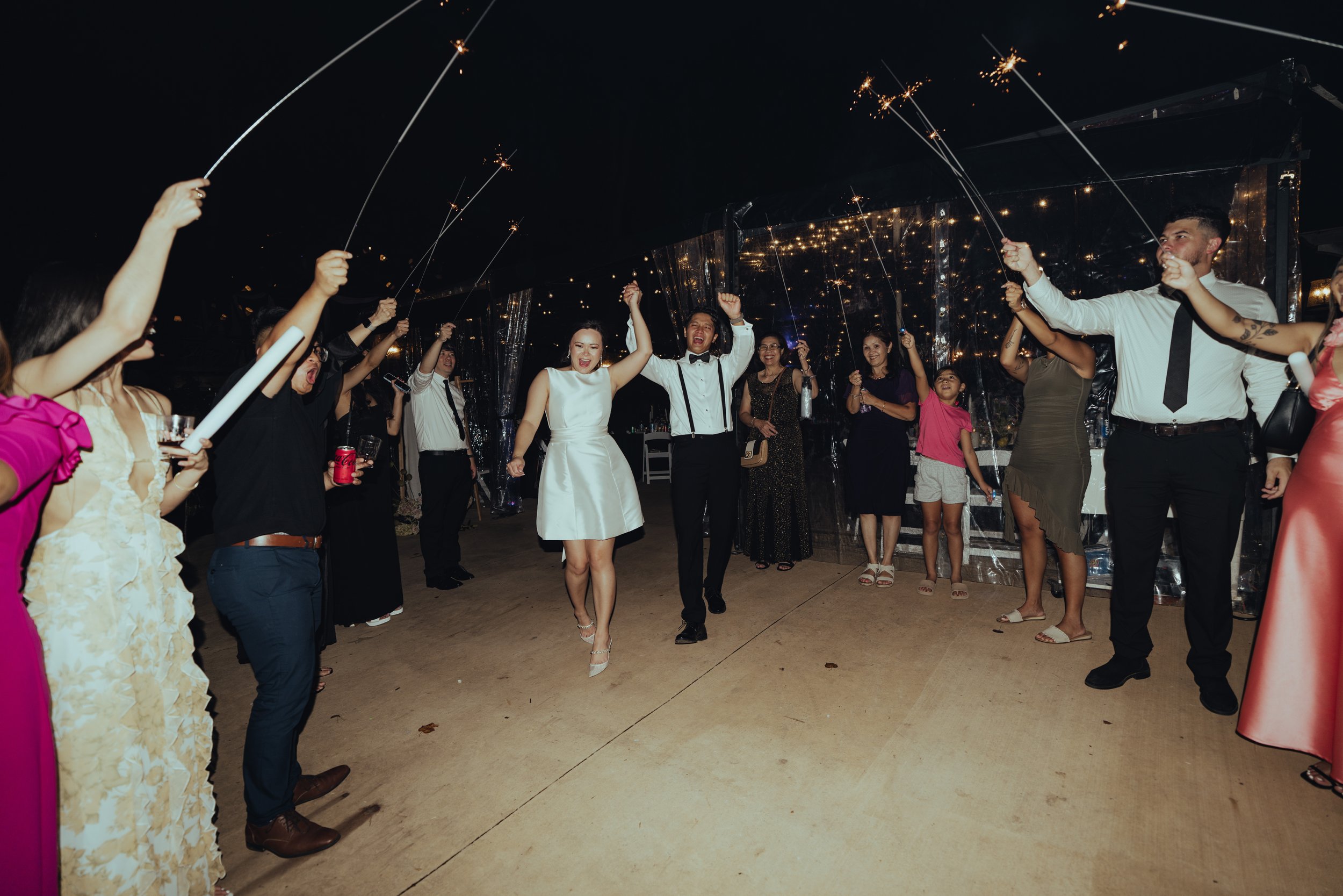 People at a celebration holding sparklers, dancing, and smiling inside a decorated venue at night.