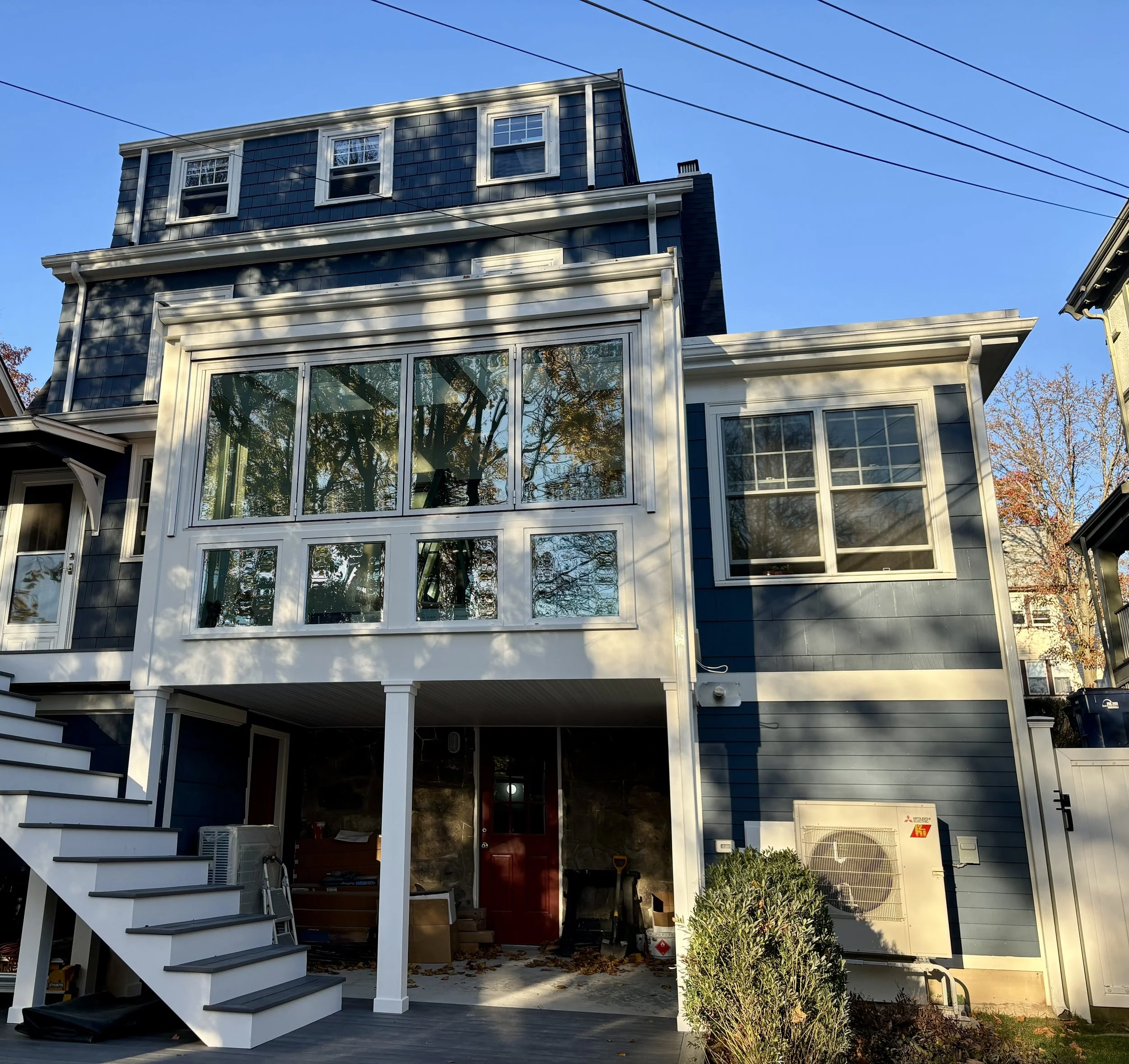 Three-story blue house with white trim, large enclosed porch, upstairs windows, on a clear day.
