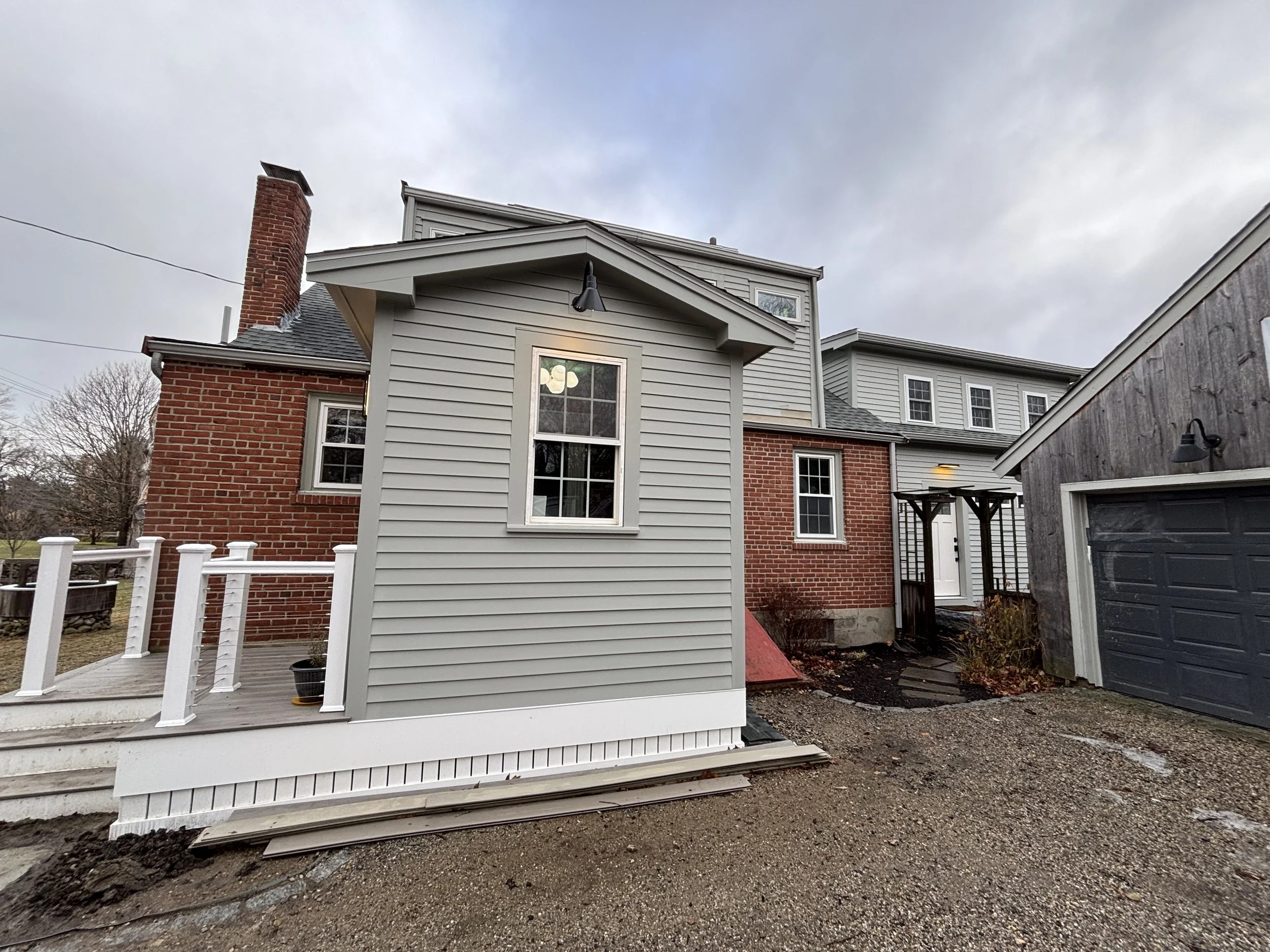 Exterior view of a modern house with a combination of brick and vinyl siding, a small deck with white railing, and a gray garage door. Overcast sky.