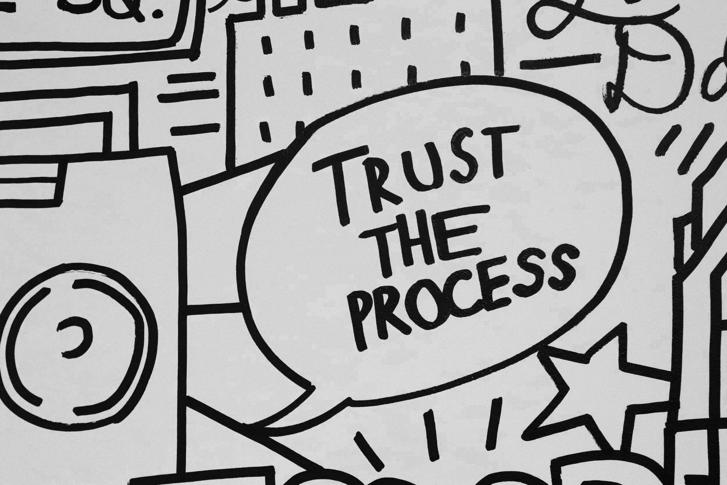 Photo of a black and white grafittied wall in the Juno office with a speech bubble that says "Trust the Process"