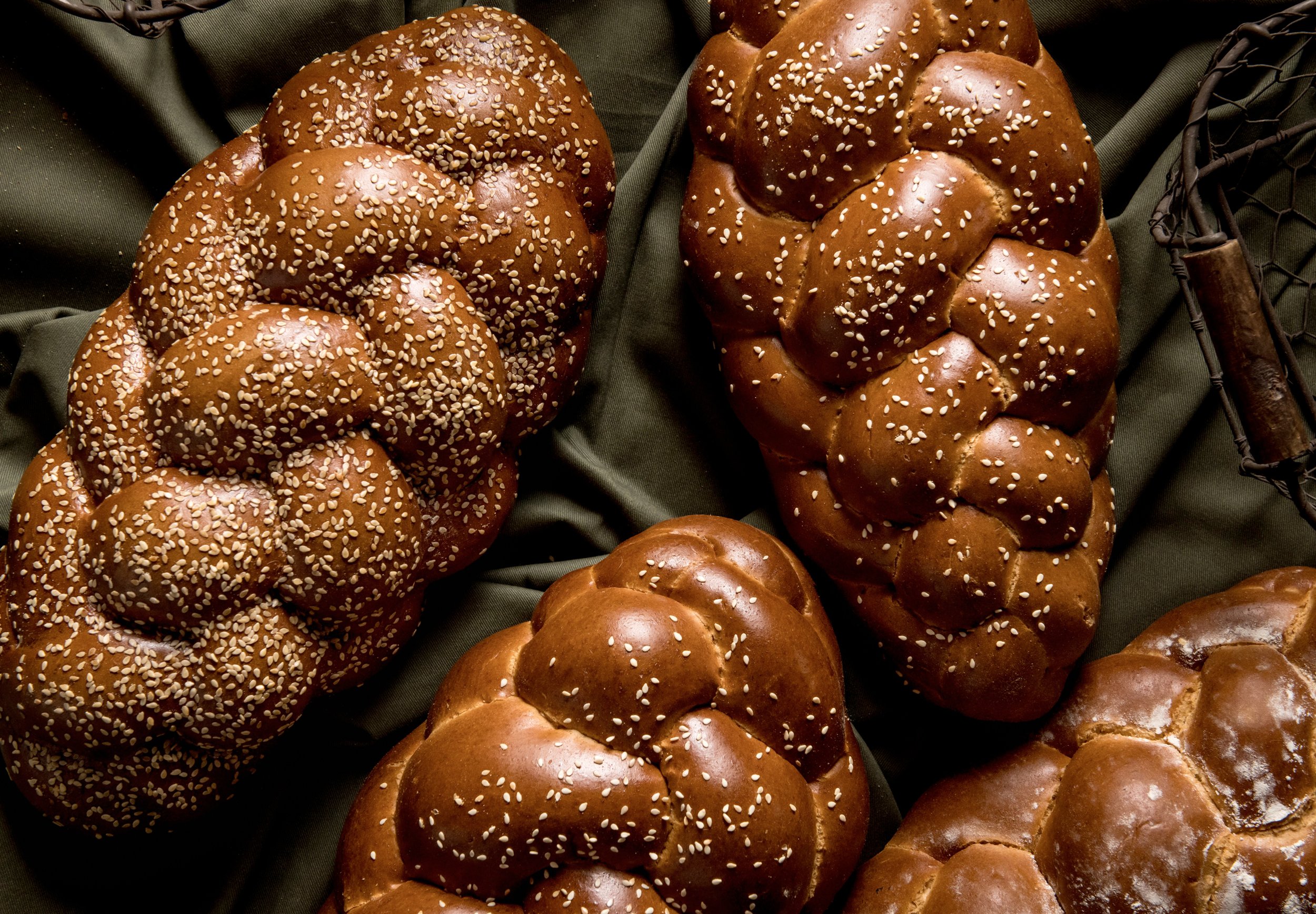 Several braided loaves of bread sprinkled with sesame seeds on a dark surface.