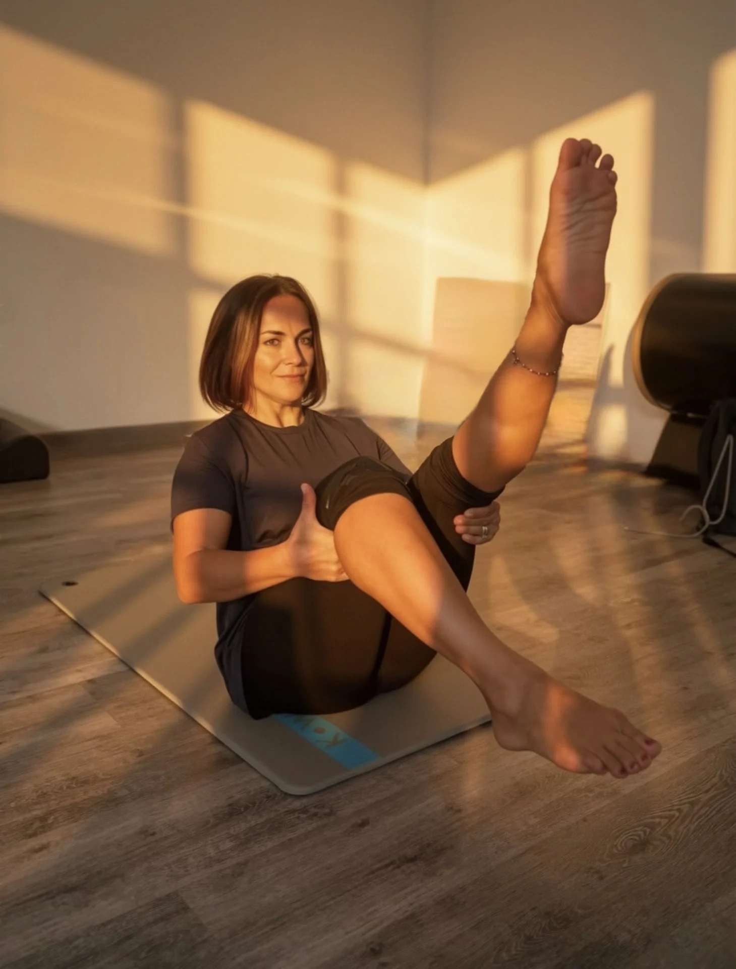 Una donna sta praticando yoga o stretching in una stanza con luci calde e ombre create da una finestra.