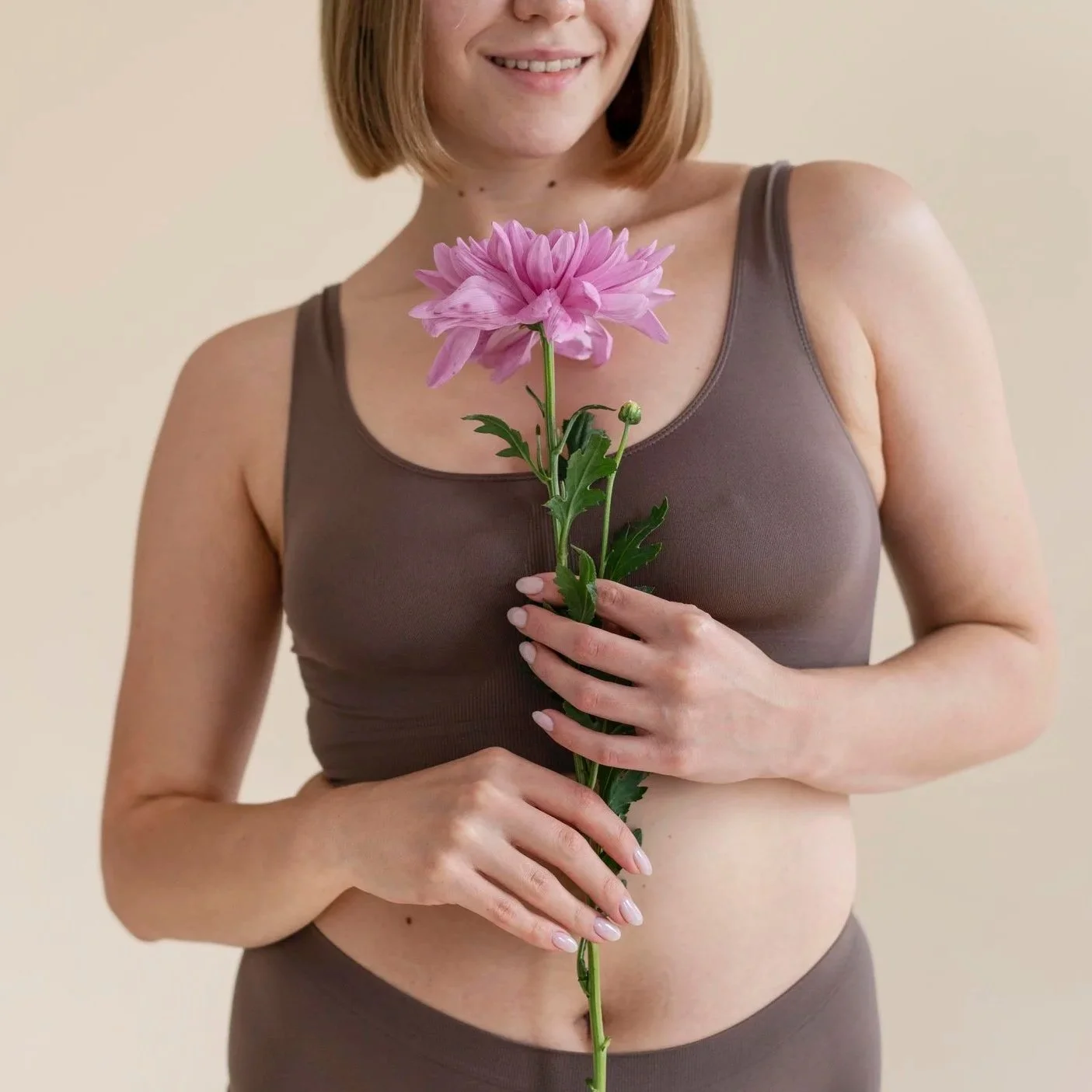 Donna con capelli corti, sorriso, indossa una canotta marrone e tiene una rosa viola con foglie verdi.