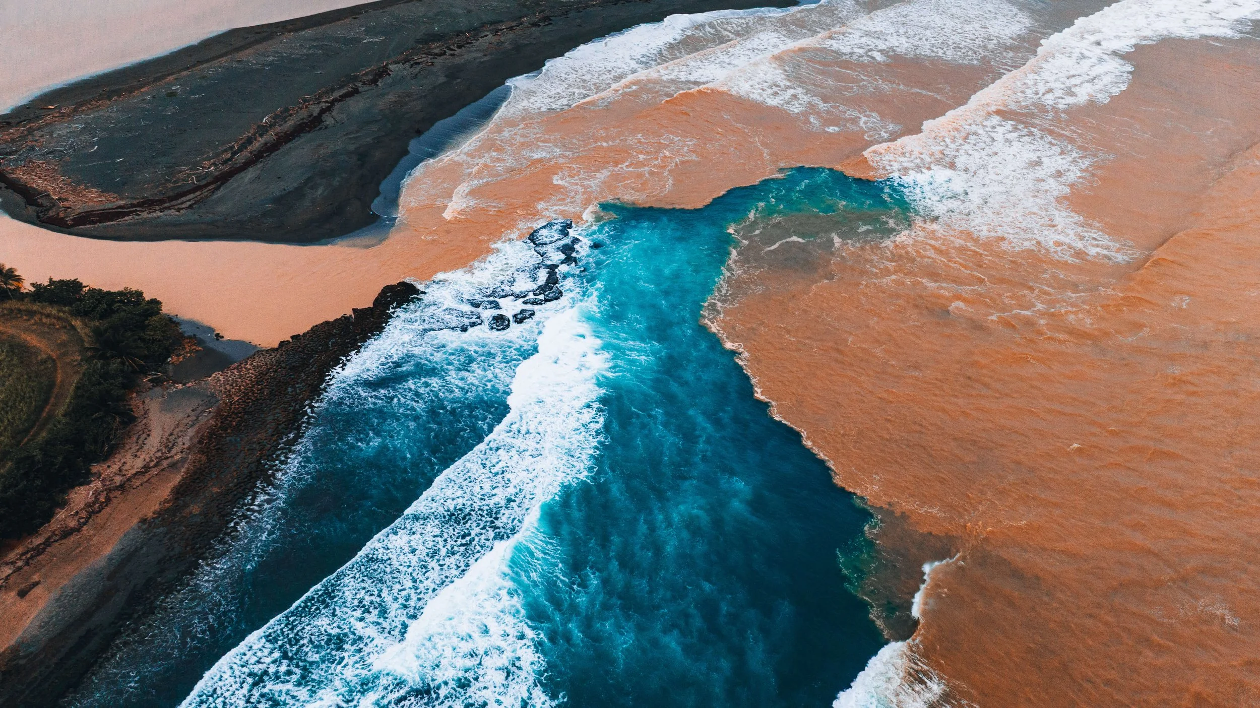 Aerial view of the shoreline where the ocean meets the beach, with waves crashing onto the sandy coast.
