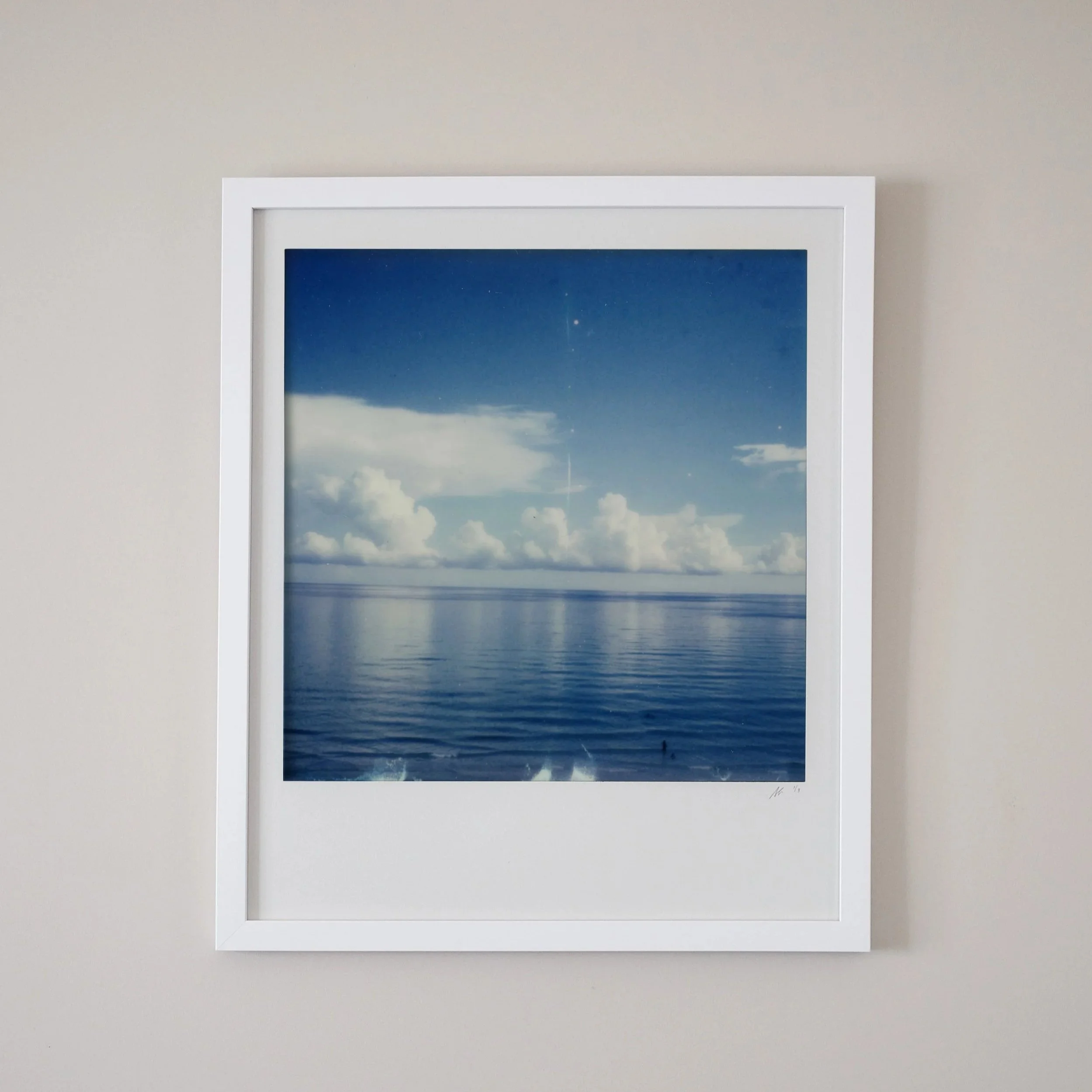 Framed photograph of a blue sky with clouds over a calm ocean, with faint stars visible.