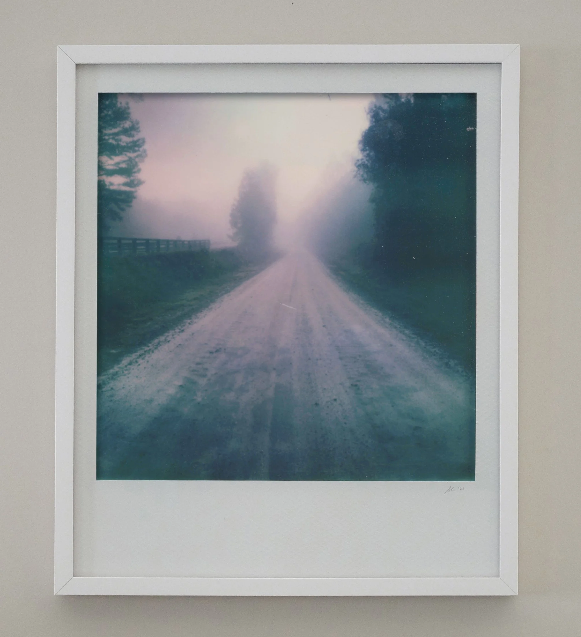A framed photograph of a foggy dirt road flanked by trees and a fence, with a hazy sky.