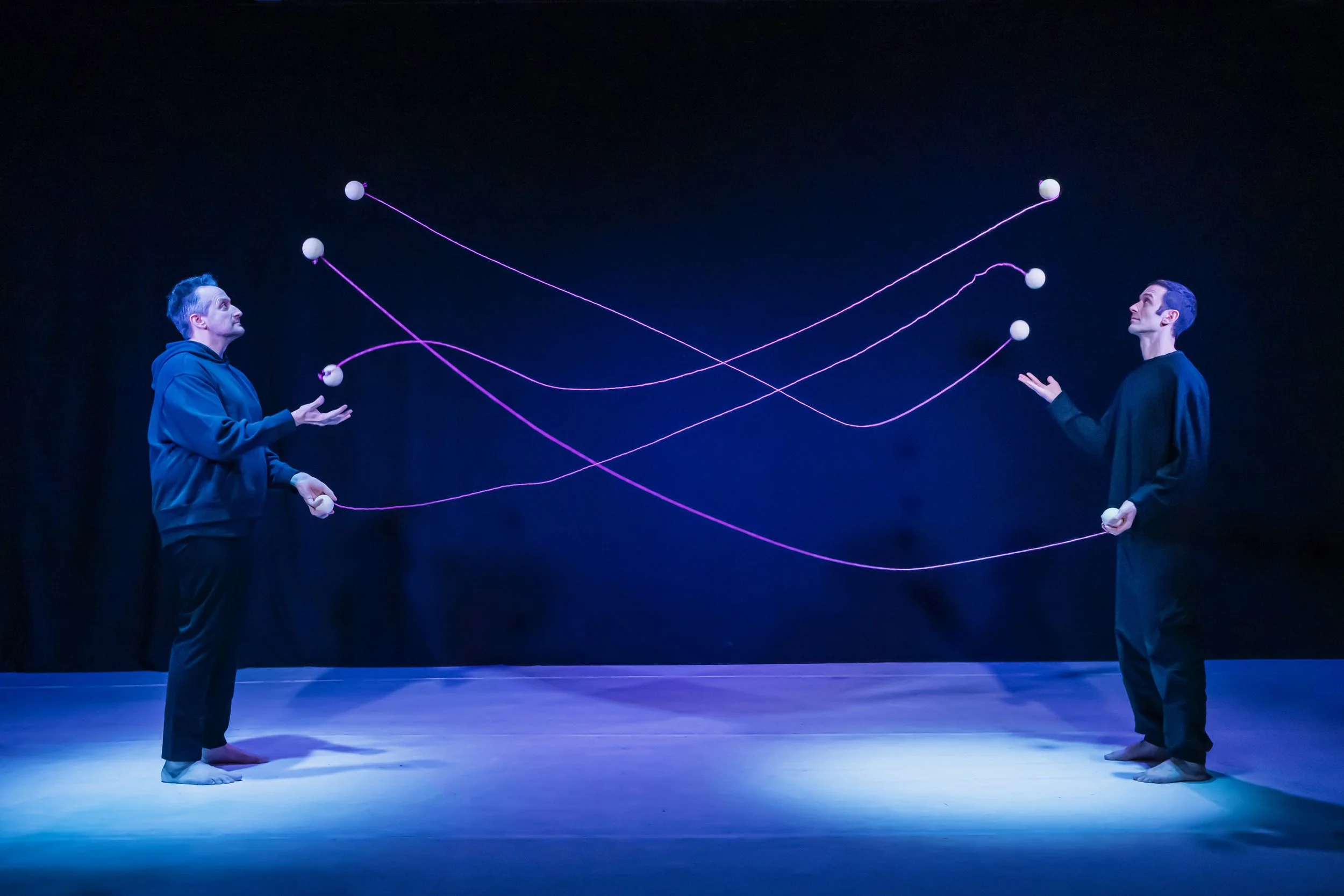 two jugglers share 4 balls each with string connecting the patterns